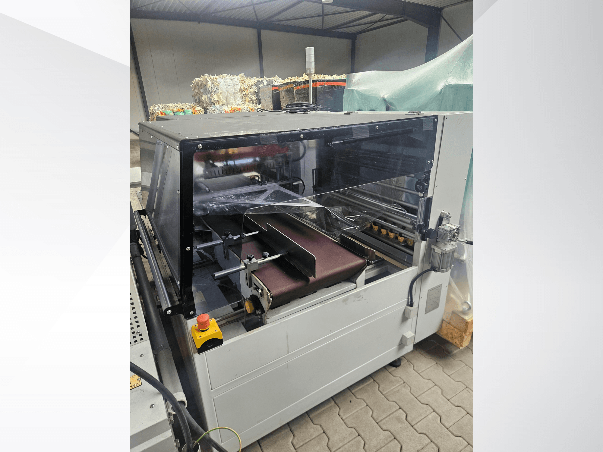 AMTEC Speed Shrink 40 PRO-maskin, framifrån, som visar en plastbearbetningsmekanism med ett genomskinligt skyddshölje och ett transportband.
