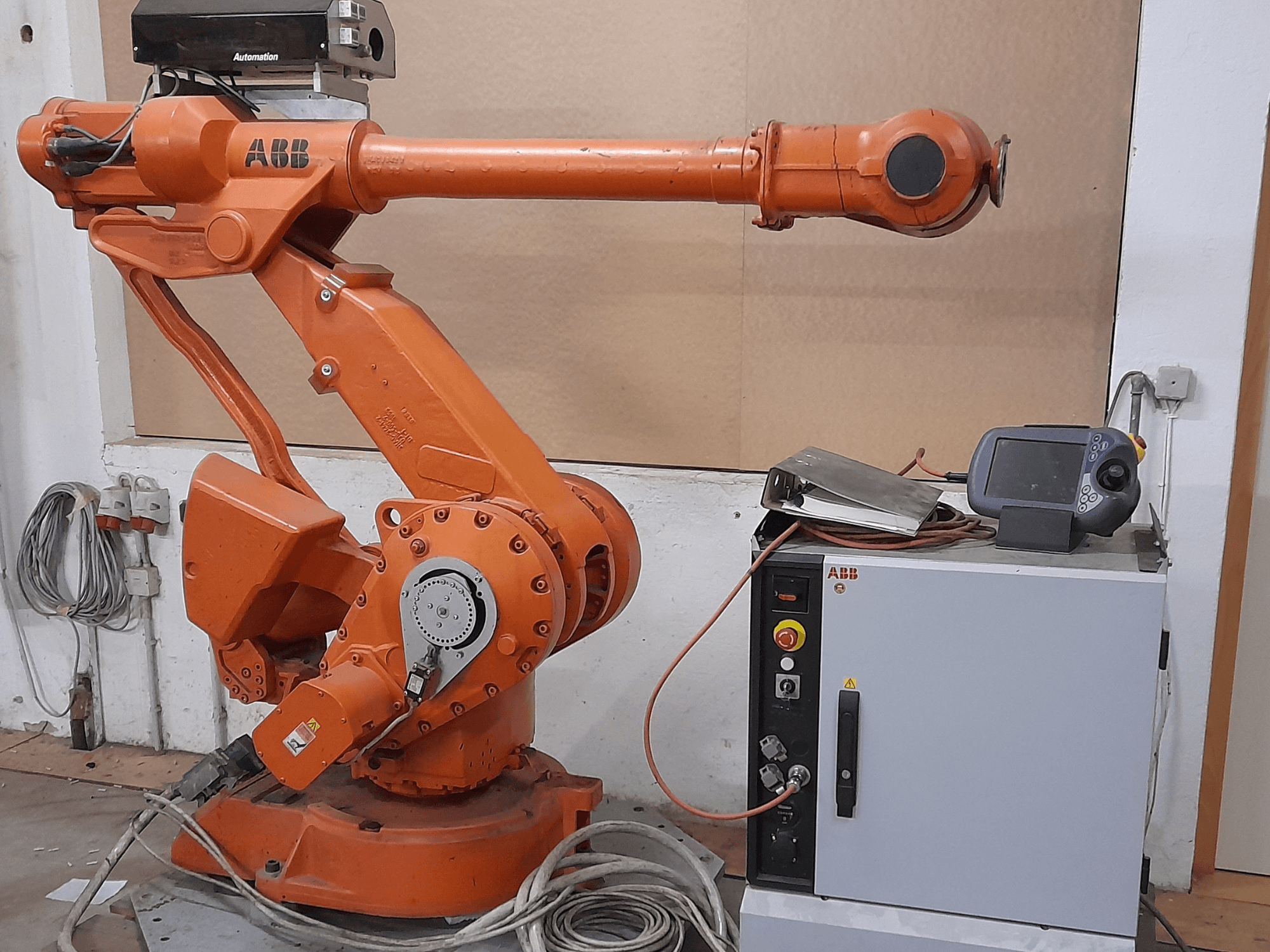 Orange ABB-robotarm med kontrollpanel, framifrån, som visar kablar och automationsutrustning.