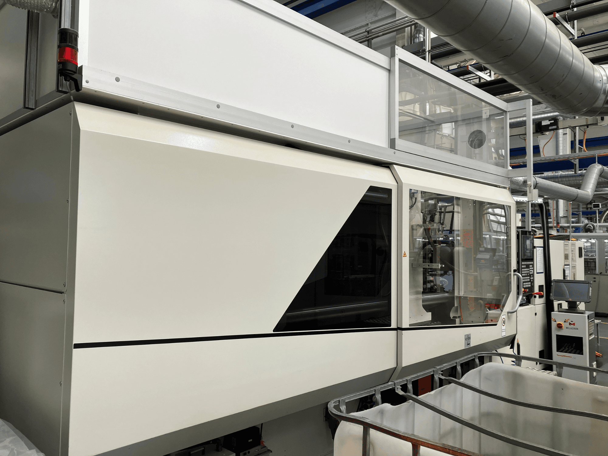 Industrimaskinens framsida, med en elegant vit design, displaypanel och glasparti för synlighet av komponenter.