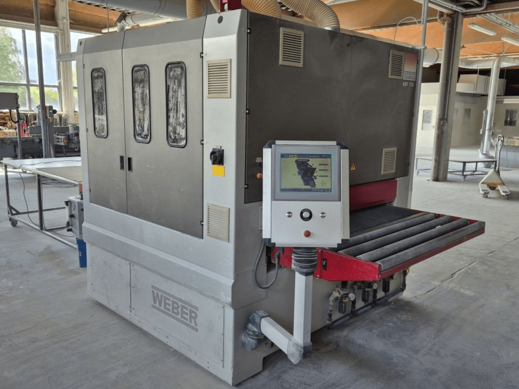 WEBER KSF-3-1350 bandslipmaskin, sidovy som visar reglage, strömpanel och sliptransportör. Industriell miljö med synliga maskiner.