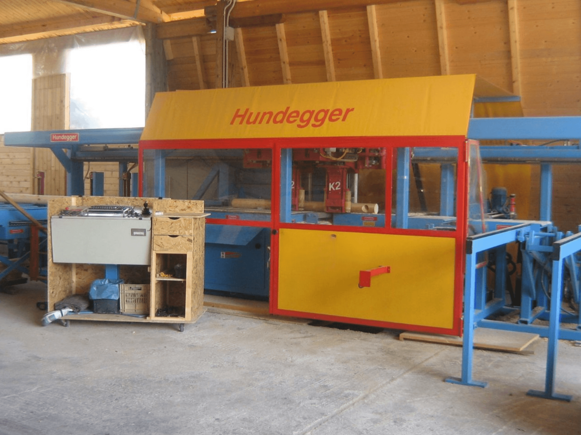 CNC-bearbetningscenter för trä HUNDEGGER K2 4 assi i en verkstad, framifrån med gul och blå design och arbetsbord.