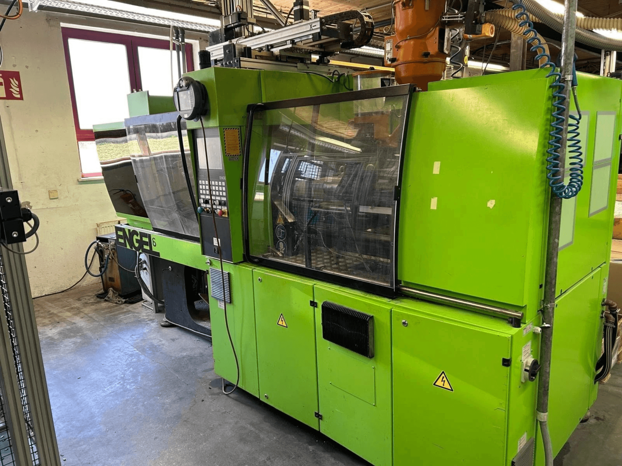 Framifrån sett på den hydrauliska formsprutningsmaskinen Engel VICTORY 330/80 Tech, med grön yttre finish och kontrollpanel.