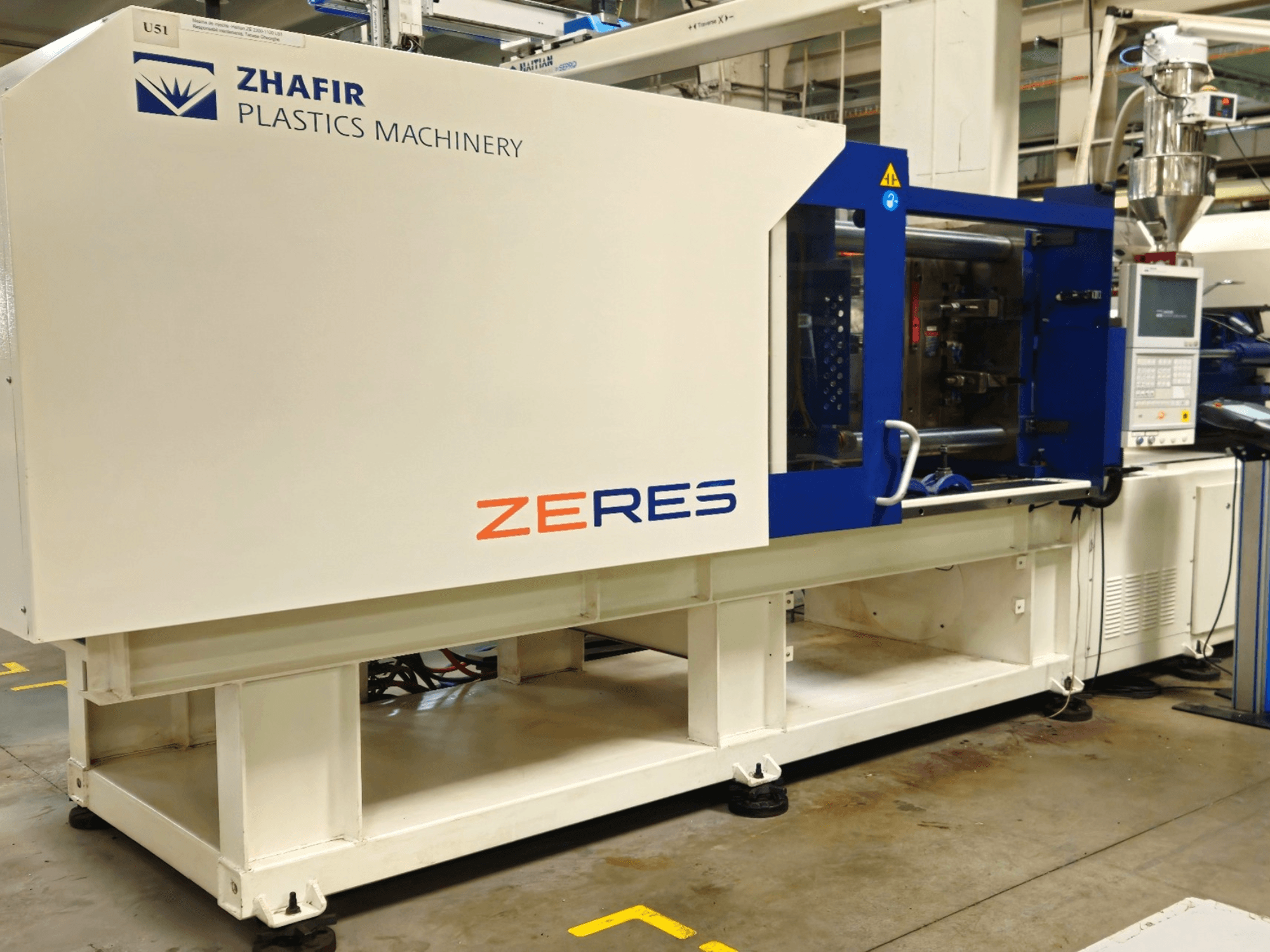 Zhafir Zeres plastformsprutningsmaskin, sidovy, visar kontrollpanel, tratt och elegant vit/blå design.