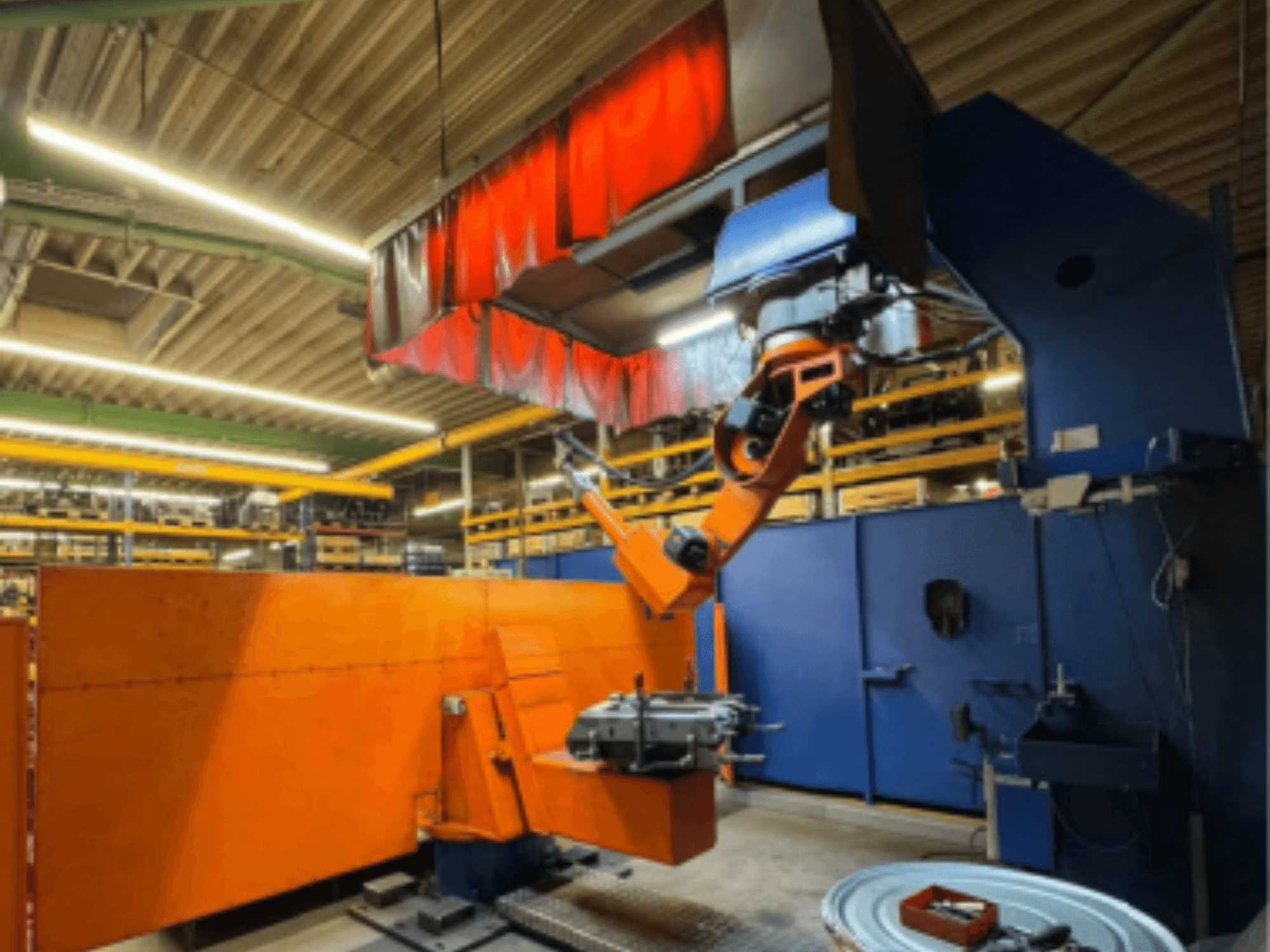 CLOOS Romat 350 e svetsrobot i en industriell miljö, framifrån med orange arm, håller ett arbetsstycke under takridå.