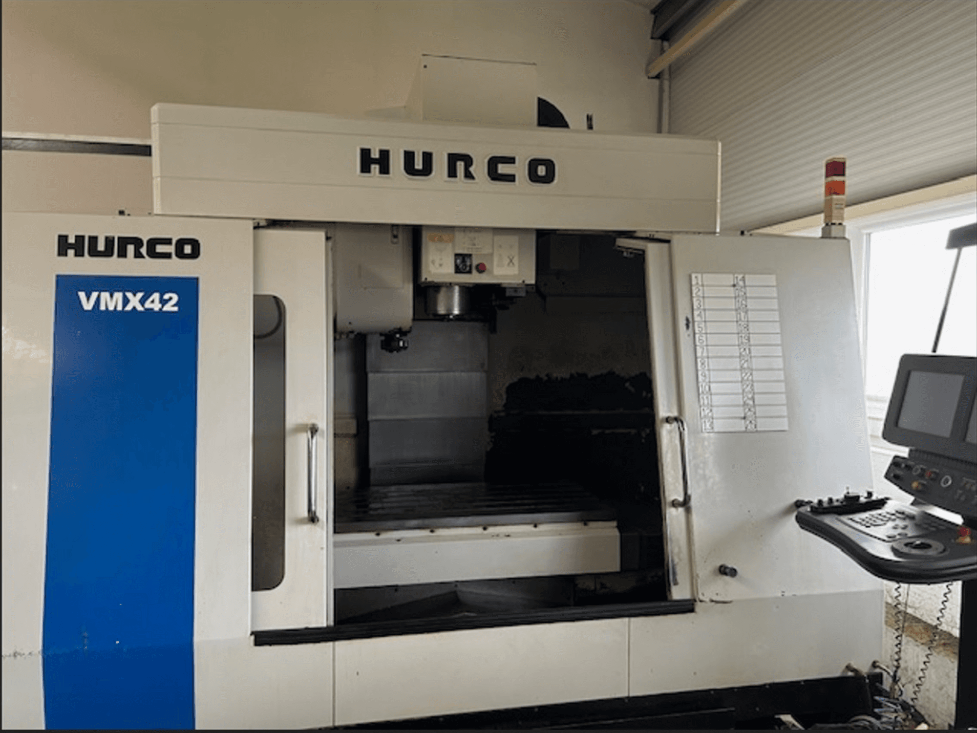 Hurco VMX42 CNC-fräsmaskin, framifrån, med kontrollpanel och öppen arbetsyta för bearbetningsoperationer.