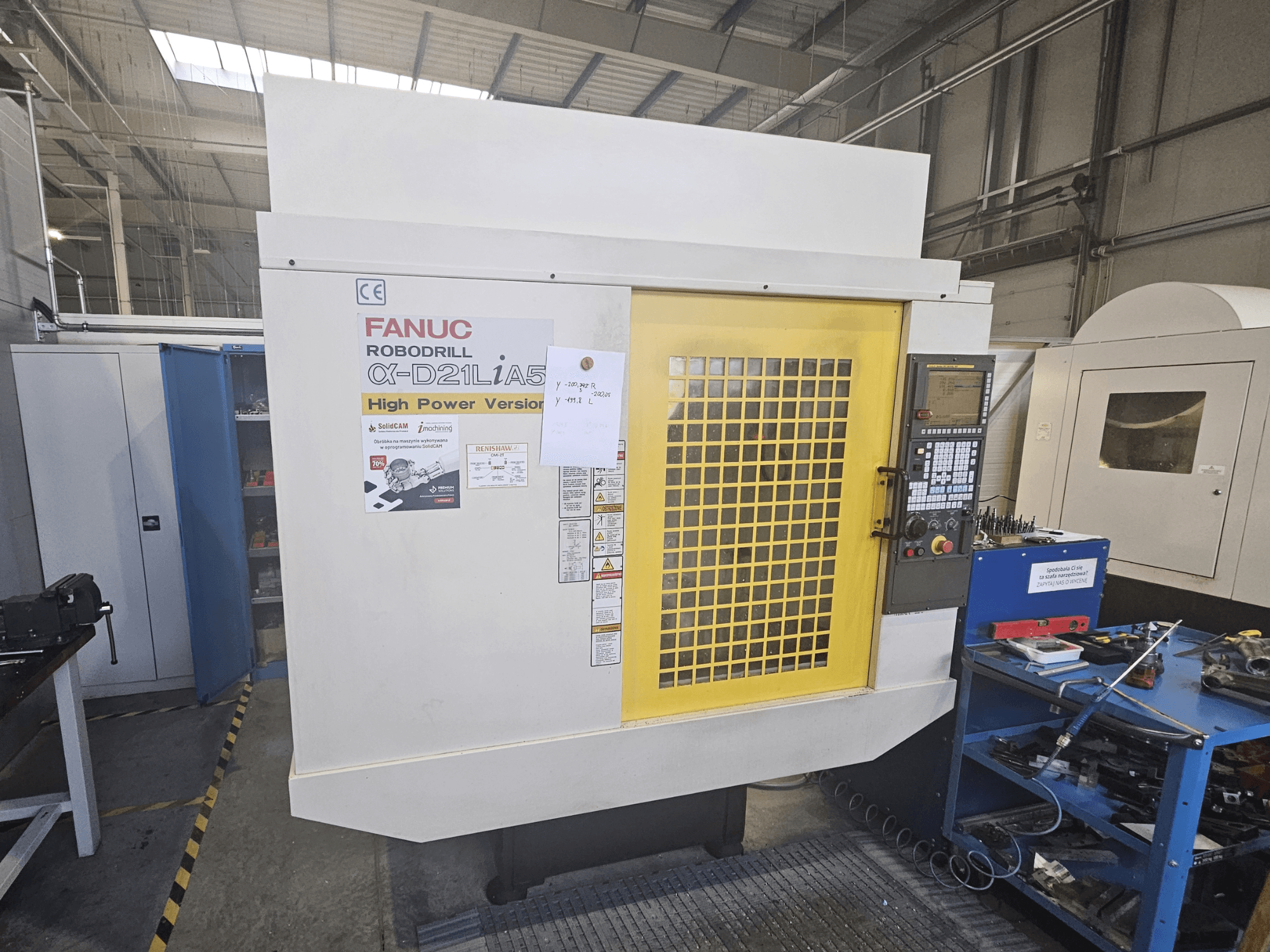 Frontvy av en FANUC Robodrill α-D21LiA5 med gul säkerhetsdörr, kontrollpanel och arbetsverktyg i närheten.
