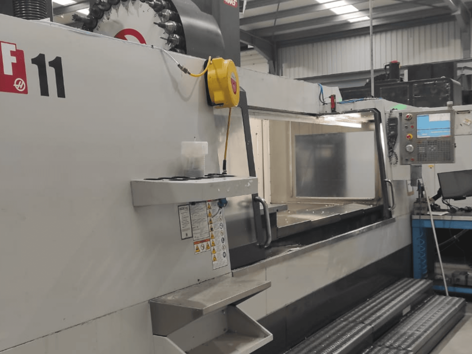 Maskin från Haas, modell VF-11, visad framifrån med kontrollpanel, stort arbetsområde och säkerhetsetiketter synliga.