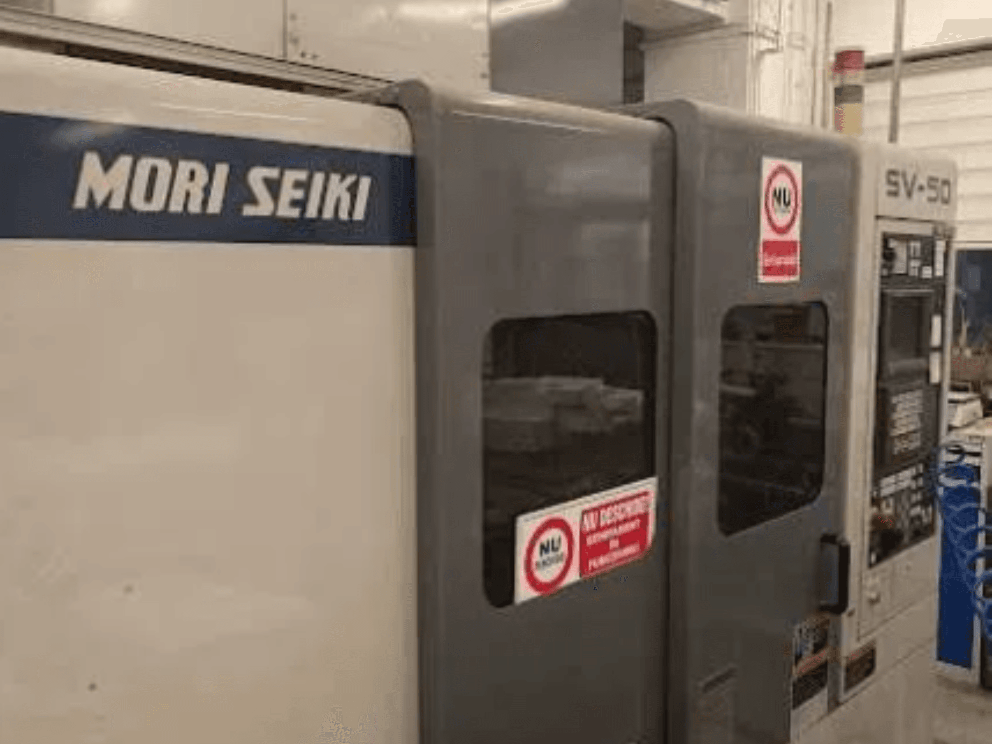 MORI SEIKI SV-50 CNC-maskin, sidovy; har kontrollpanel och dekaler med säkerhetsvarningar.