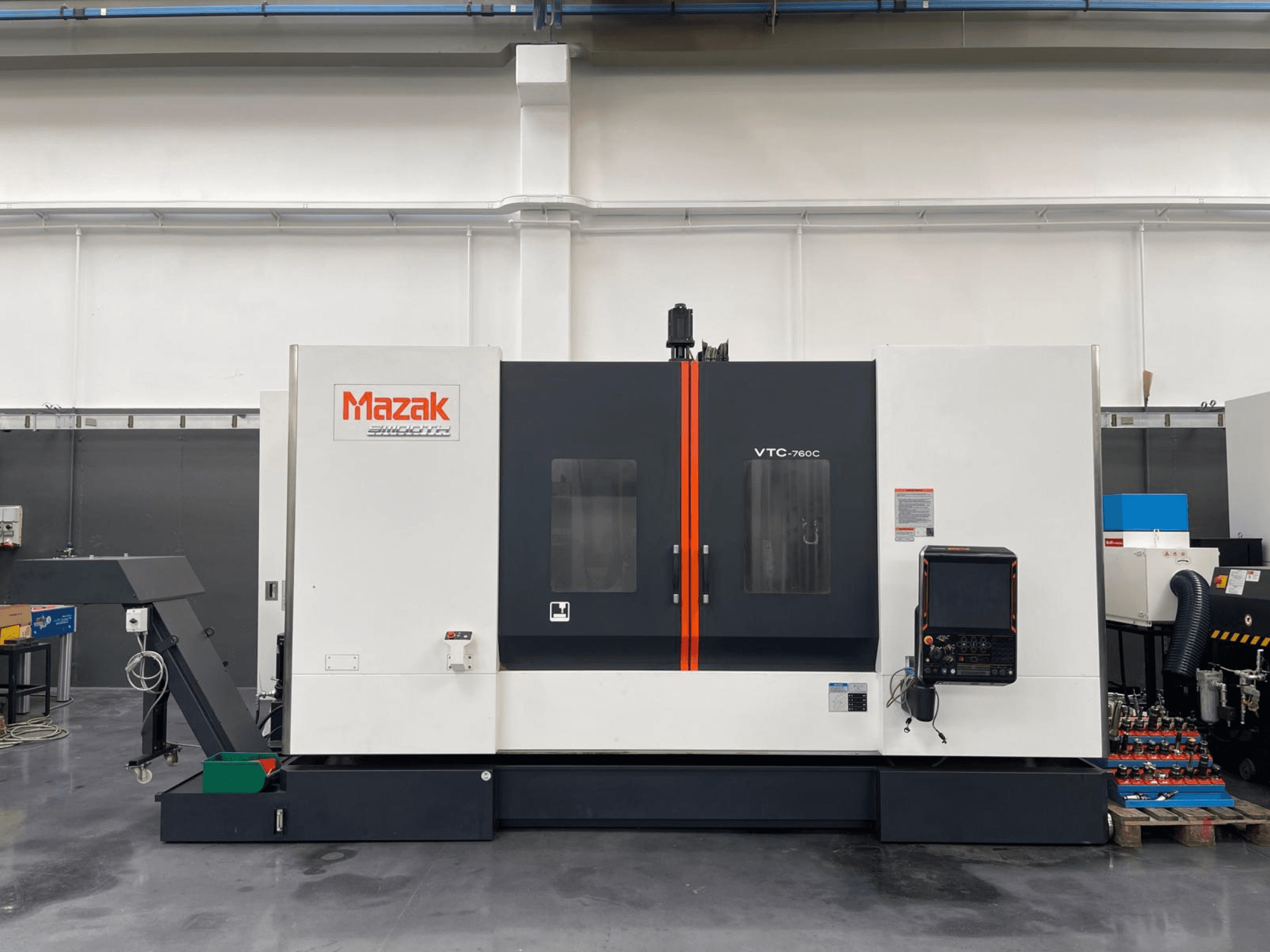 Mazak VTC 760C vertikal fleroperationsmaskin, sidovy som visar reglage, vit och svart exteriör och orangefärgade detaljer.