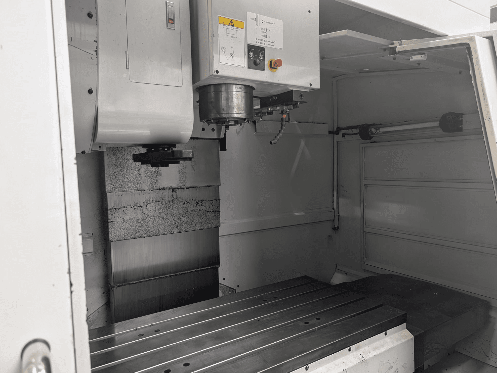 Invändig vy av en CNC-fräsmaskin med ett stort arbetsbord i metall och spindelmotor, med detaljerade komponenter och kontrollpanel.