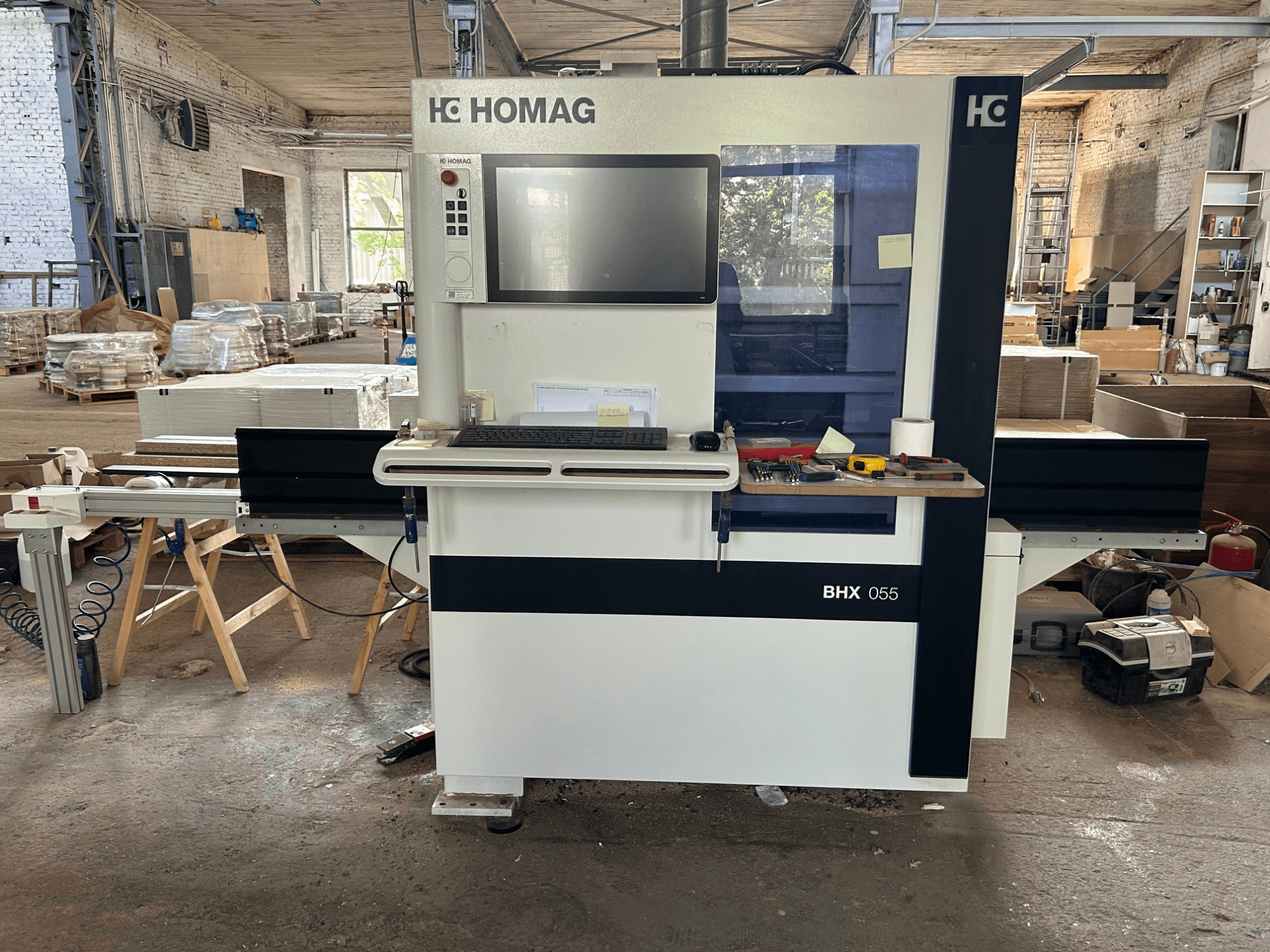 HOMAG WEEKE OPTIMAT BHX 055 CNC-bearbetningscenter, framifrån, med kontrollpanelen och arbetsytan med verktyg.