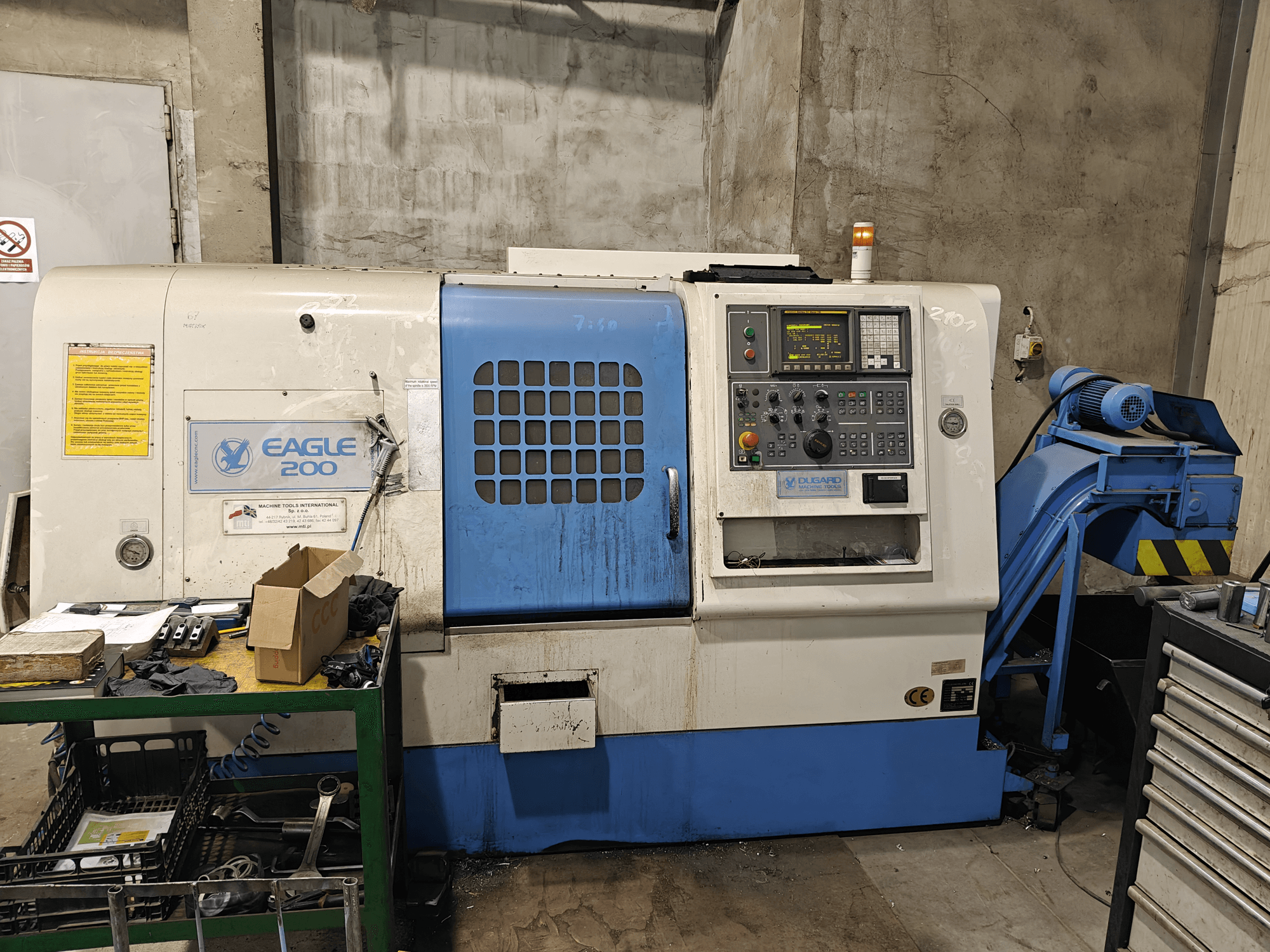 Eagle 200 CNC-maskin, framifrån med kontrollpanel, olika verktyg på en grön vagn. Synligt slitage och driftslampor.