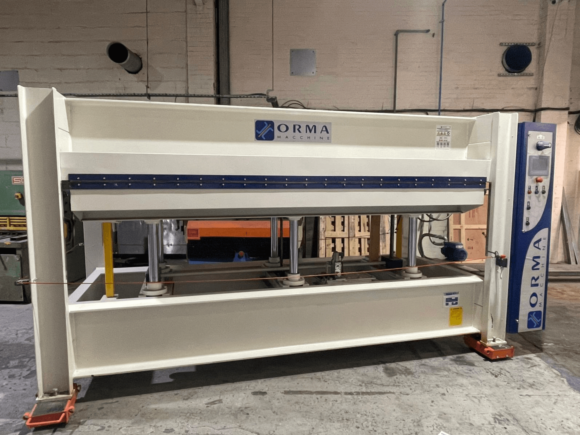 Hydraulisk press från ORMA-maskiner, framifrån, med silverfärgad yta, kontrollpanel till höger och stående kolvar för pressning.