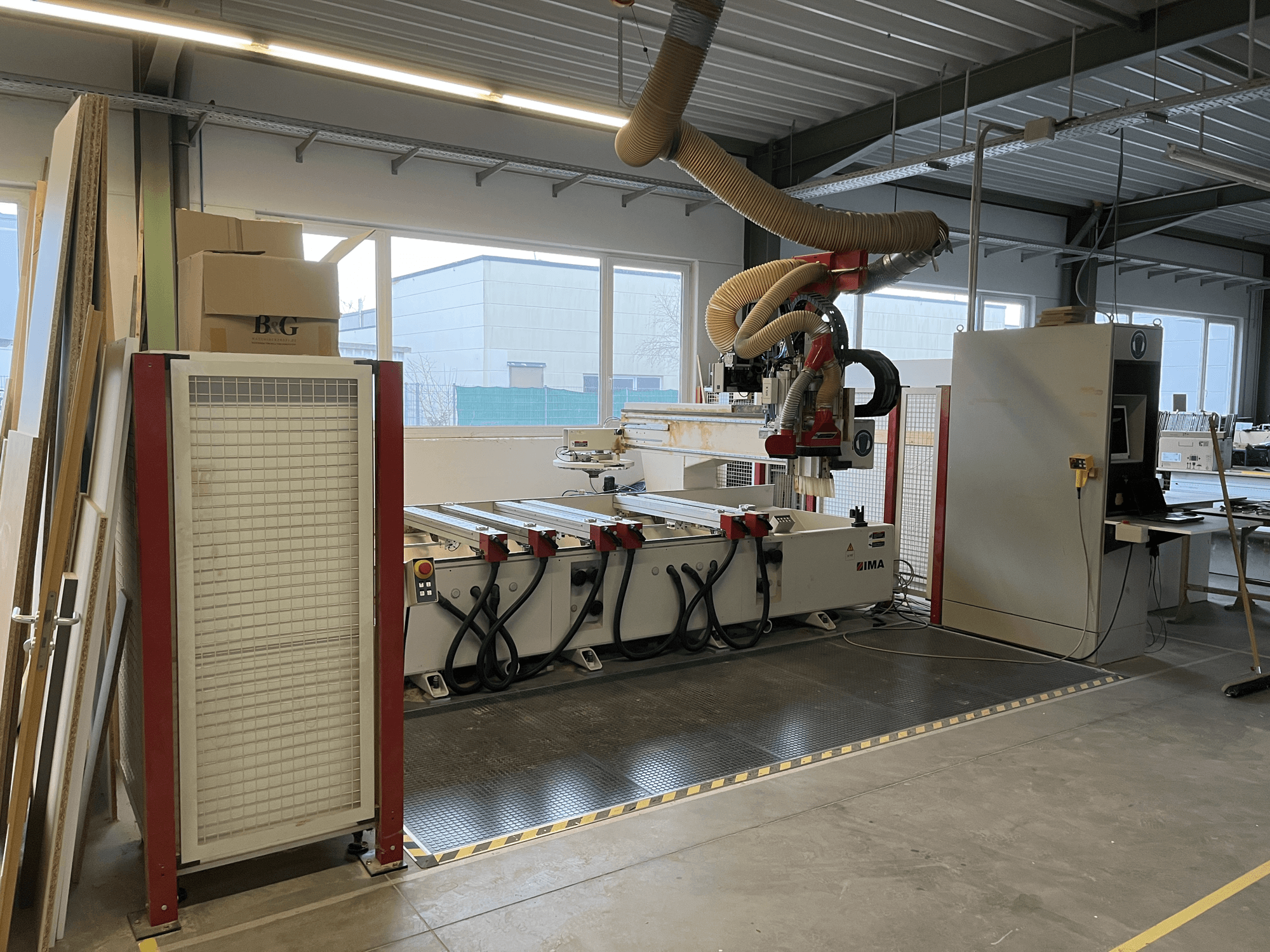 CNC-bearbetningscenter för trä IMA BIMA 410 i verkstad, sidovy med kontrollpanel och dammutsugningssystem synliga.