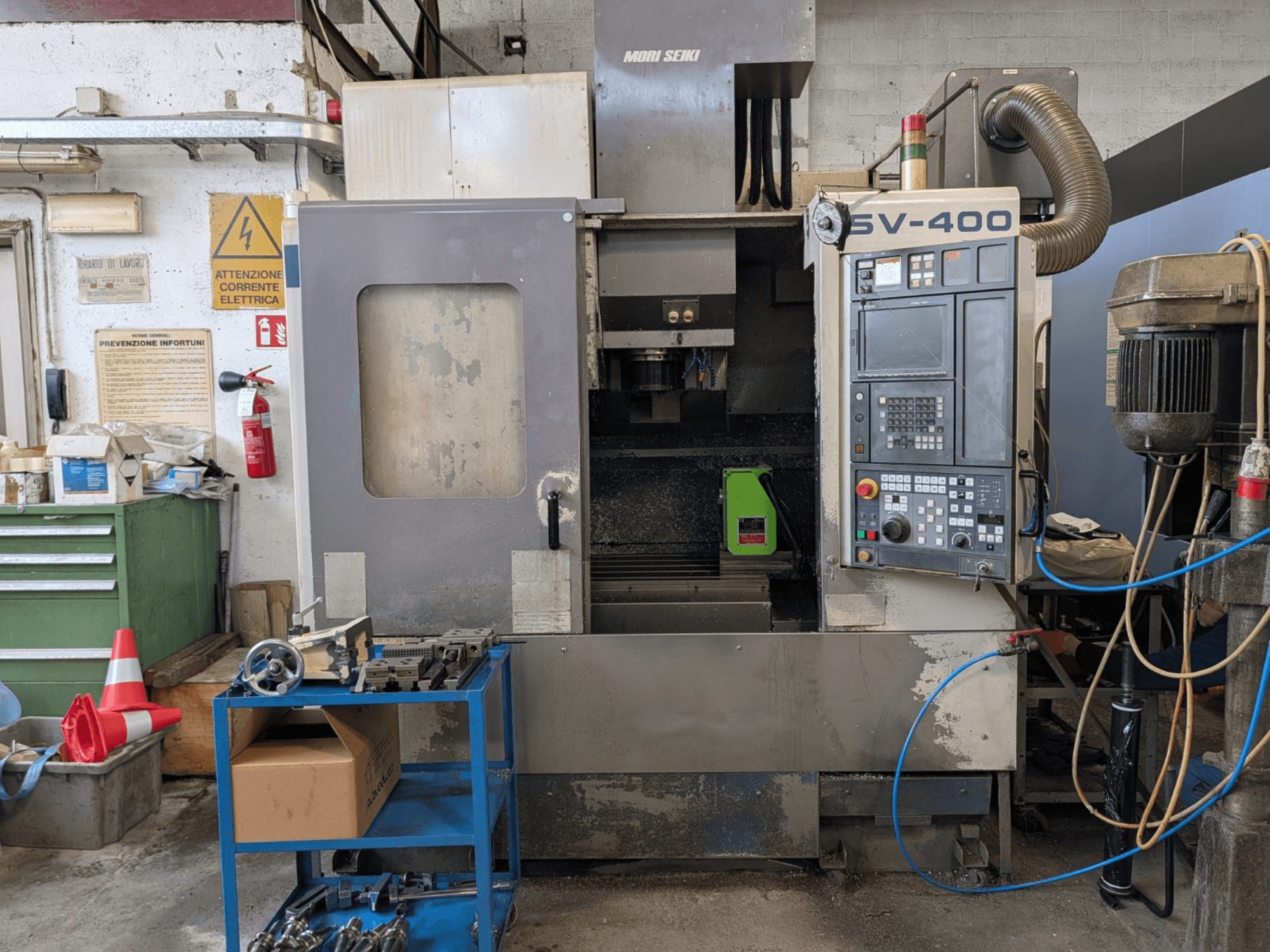 MORI SEIKI SV-400 vertikal fleroperationsmaskin i en verkstad, sidovy, visar kontrollpanelen och verktygsmaskinerna i närheten.