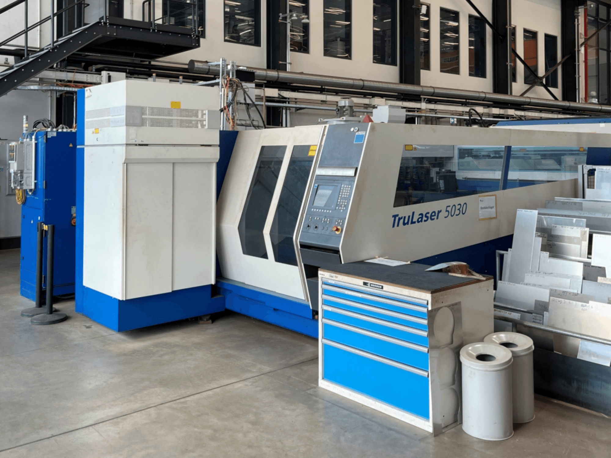 TRUMPF TruLaser 5030 CO₂-laserskärmaskin sedd framifrån, med kontrollpanel och en arbetsbänk med plåtark i närheten.