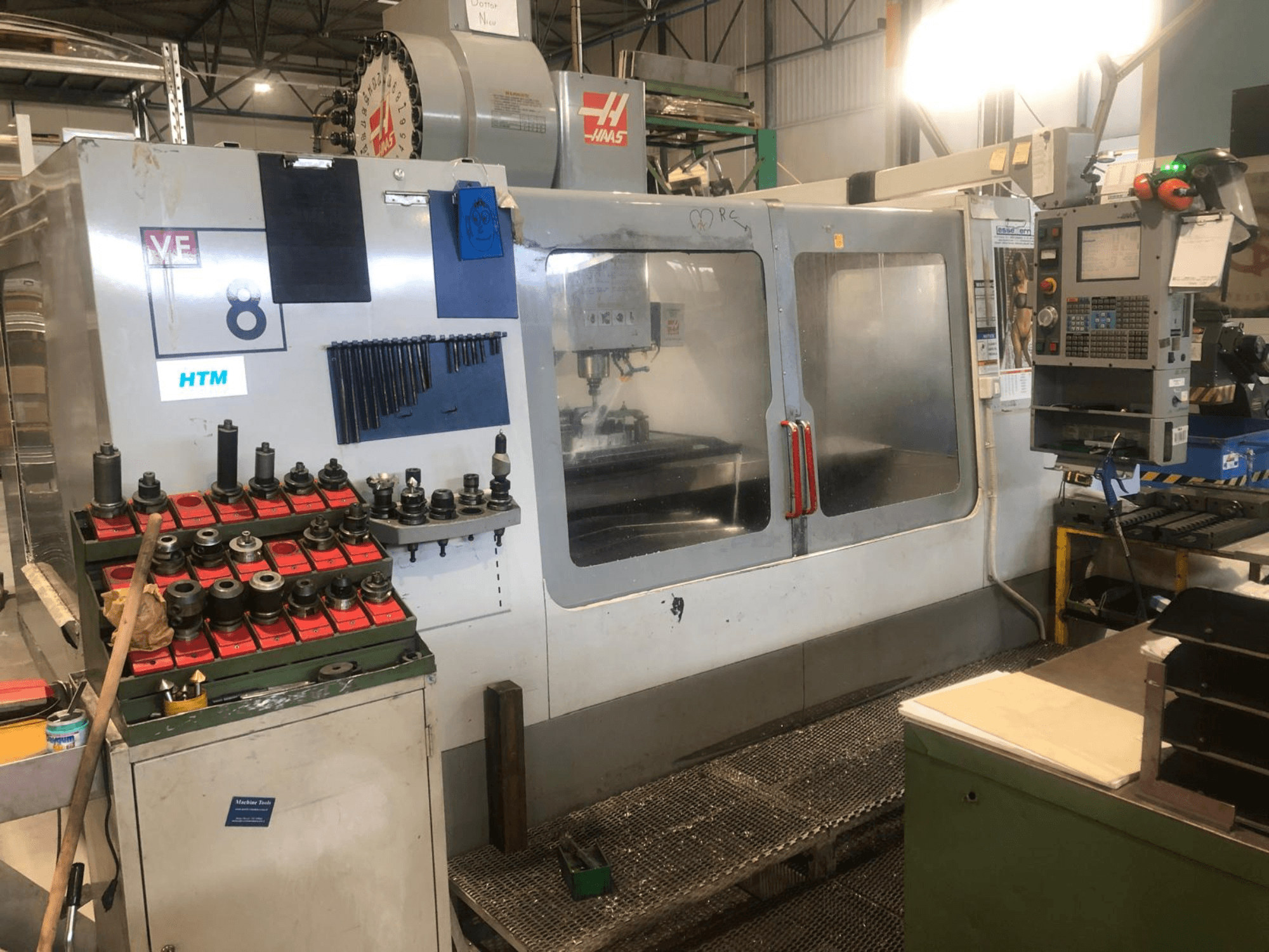 Haas CNC-maskin i en verkstad, vy framifrån; visar verktyg och reglage, med synliga modelldetaljer och organiserade verktygshållare.