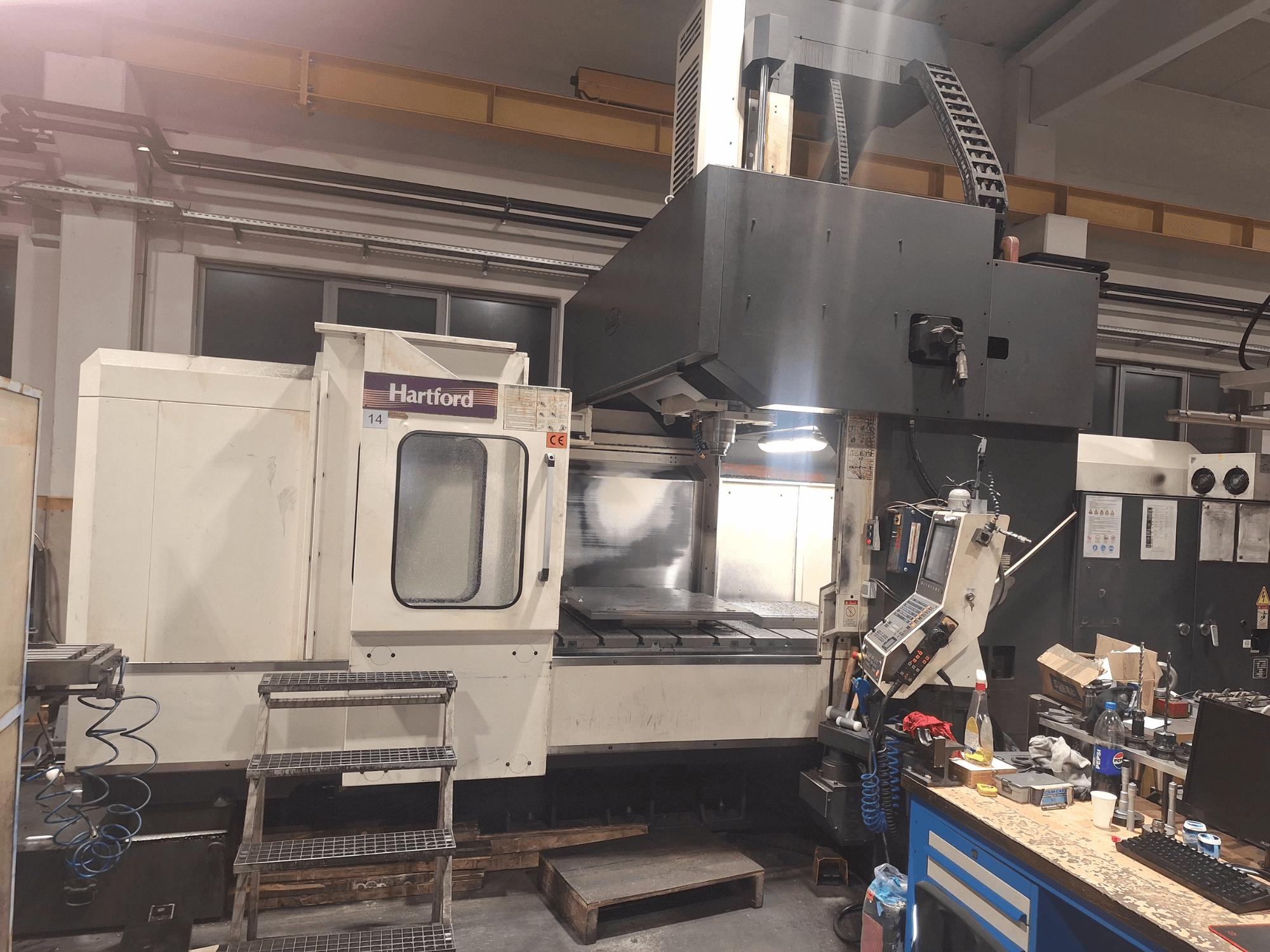 CNC-maskin från Hartford, framifrån, med tekniska reglage, steg för åtkomst och ett arbetsbord, i en verkstadsmiljö.
