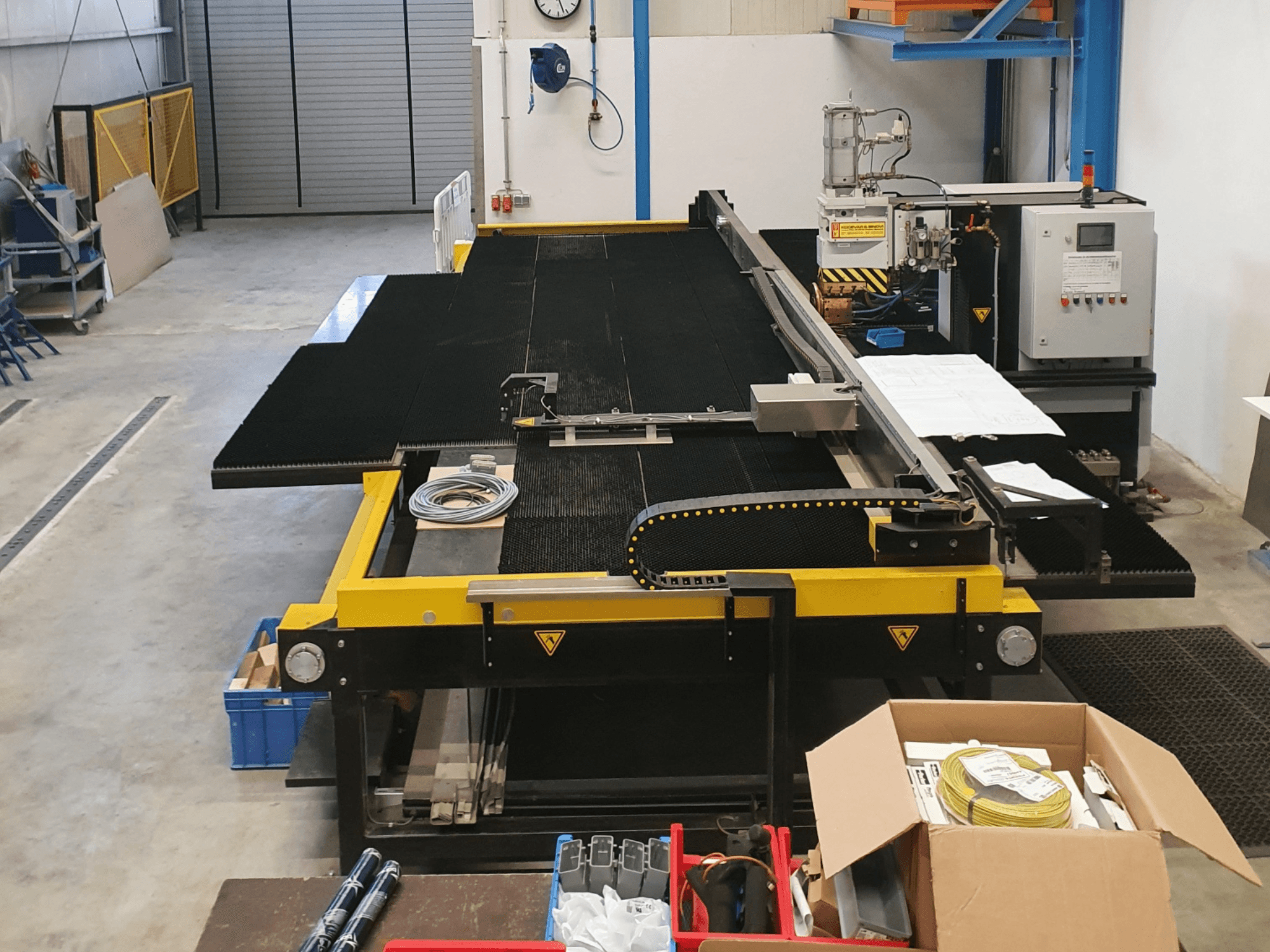 Industriell skärmaskin med gula och svarta detaljer, framifrån, visar reglage och tillbehör i en fabriksmiljö.