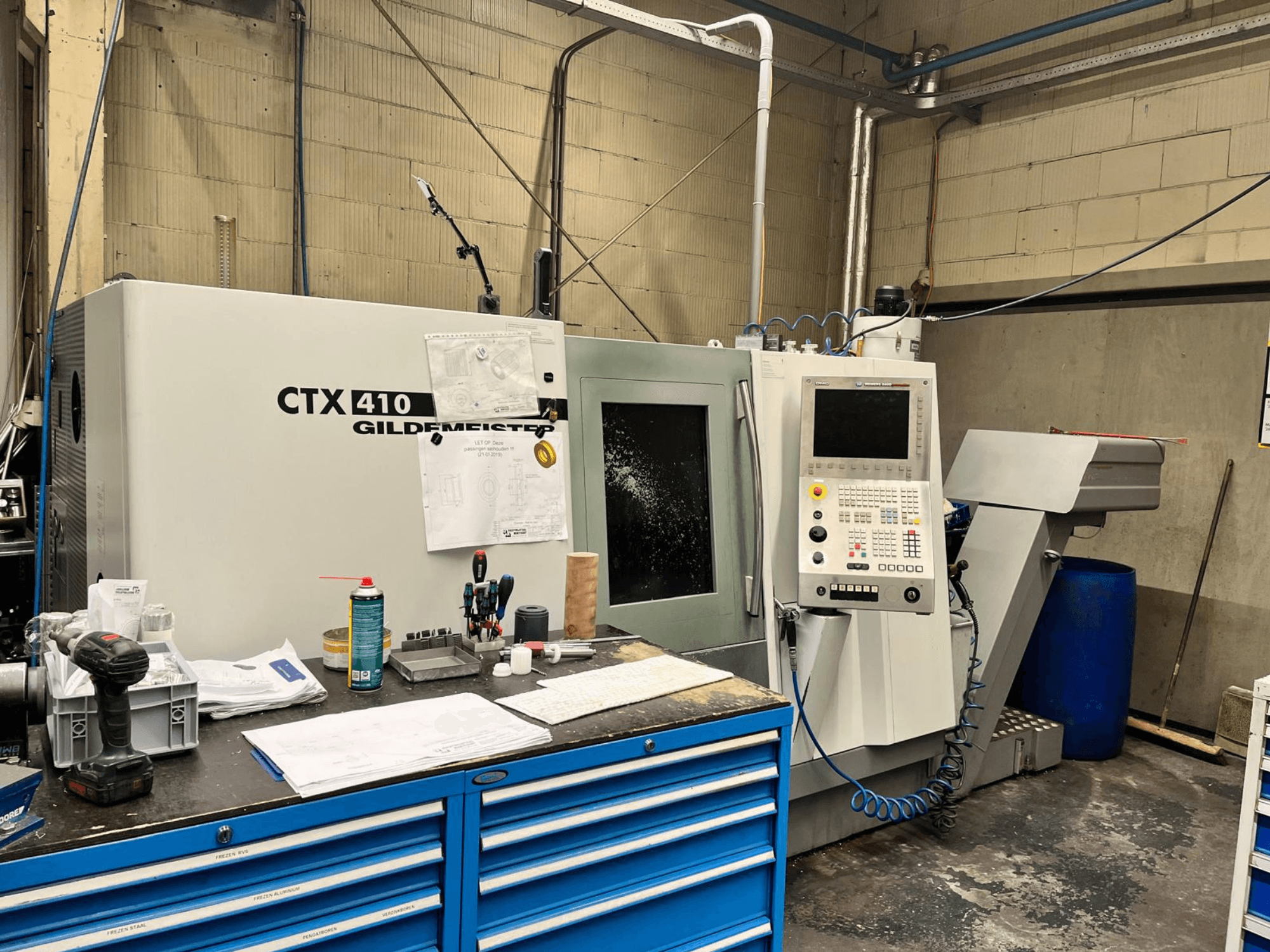 Gildemeister CTX 410 CNC-maskin i en verkstad, framifrån, med en kontrollpanel och olika verktyg på en arbetsbänk.