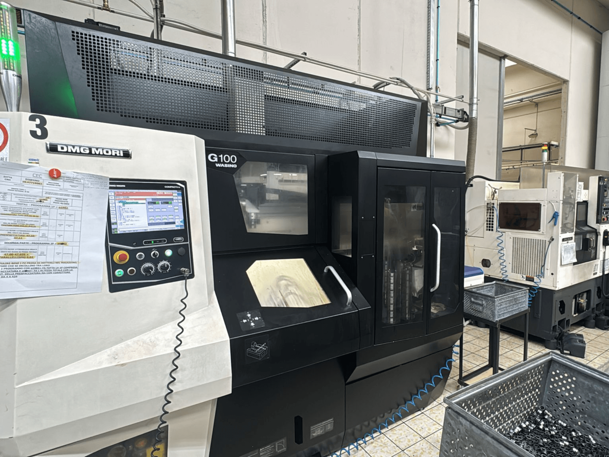 DMG MORI G100-maskin i en fabrik, framifrån, med en digital kontrollpanel och närliggande förvaringsfack för verktyg.