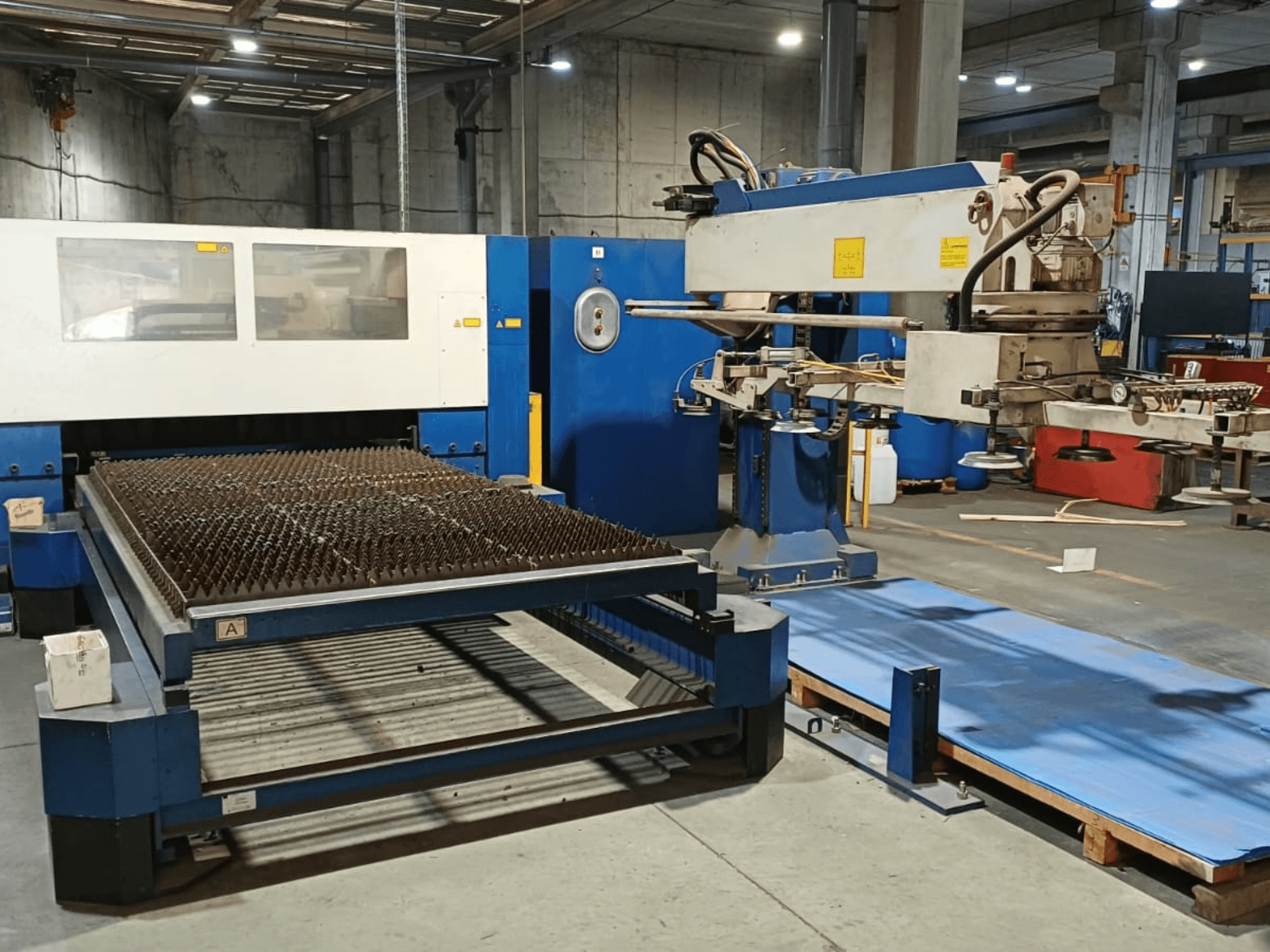 TRUMPF TRUMATIC L 3030 CO₂-laserskärmaskin, sidovy, som visar skärbordet med spikbelagd yta och robotarmen.
