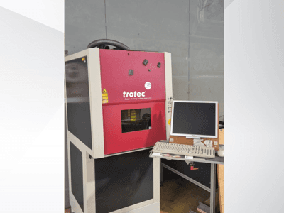En röd Trotec Laser-Work-Station sedd framifrån, med en bildskärm och ett tangentbord på arbetsstationen.