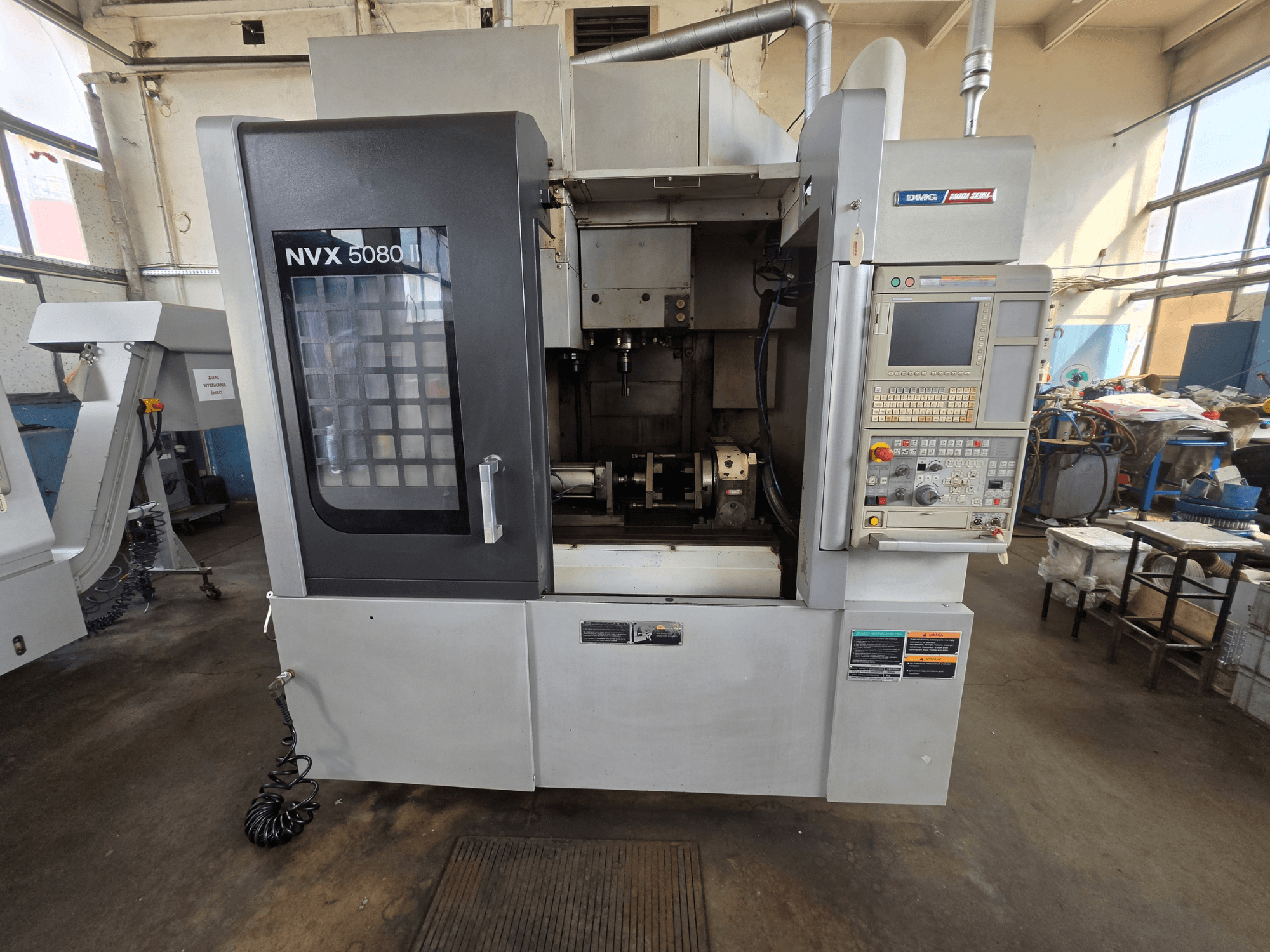 Framifrån sett på DMG Mori Seiki NVX 5080 II/40 vertikalt bearbetningscentrum med kontrollpanel och genomskinligt fönster som visar bearbetningsområdet.