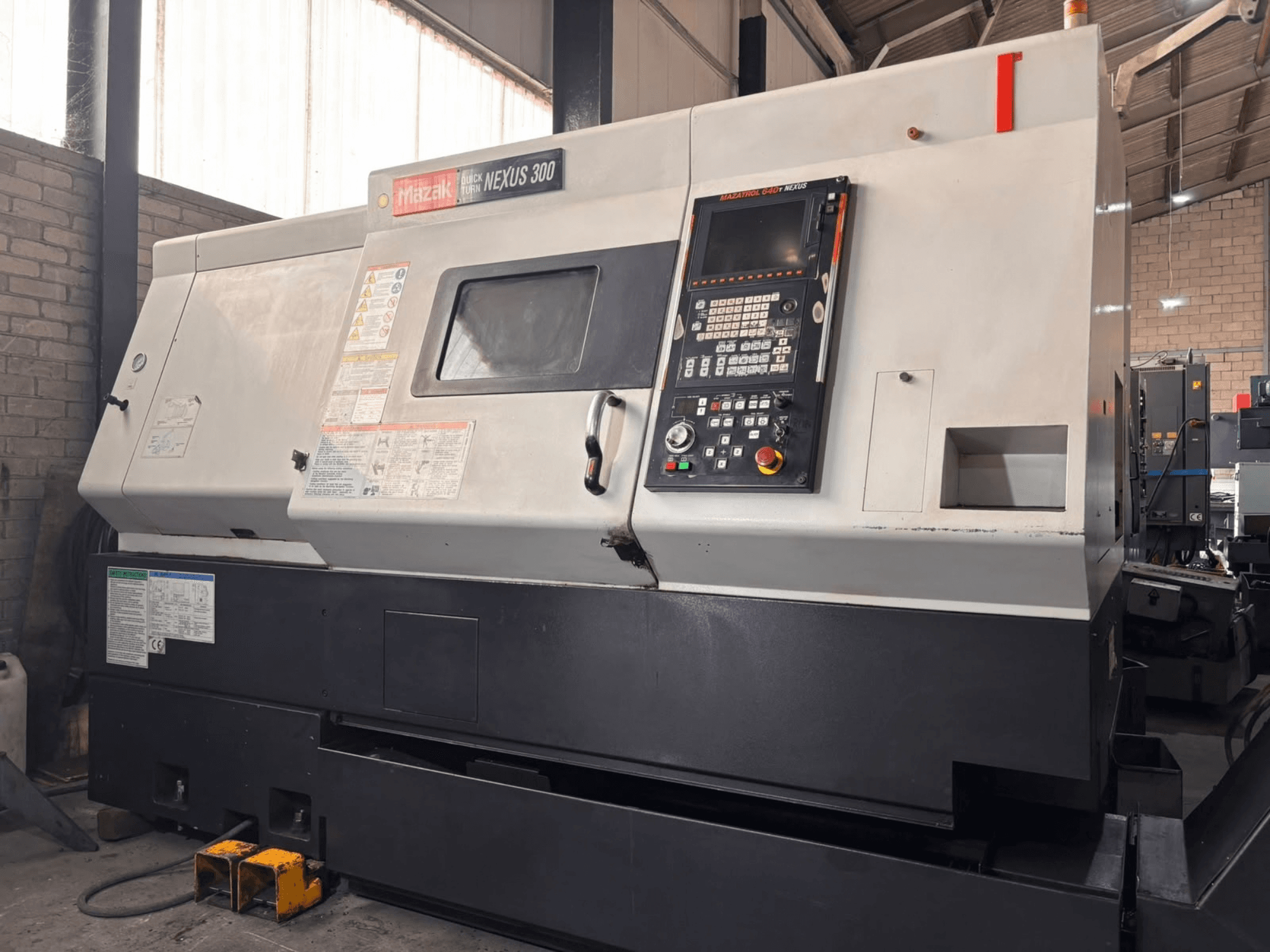 Mazak QT NEXUS 300 horisontell svarv, sidovy som visar kontrollpanelen och driftsindikatorerna i en verkstadsmiljö.
