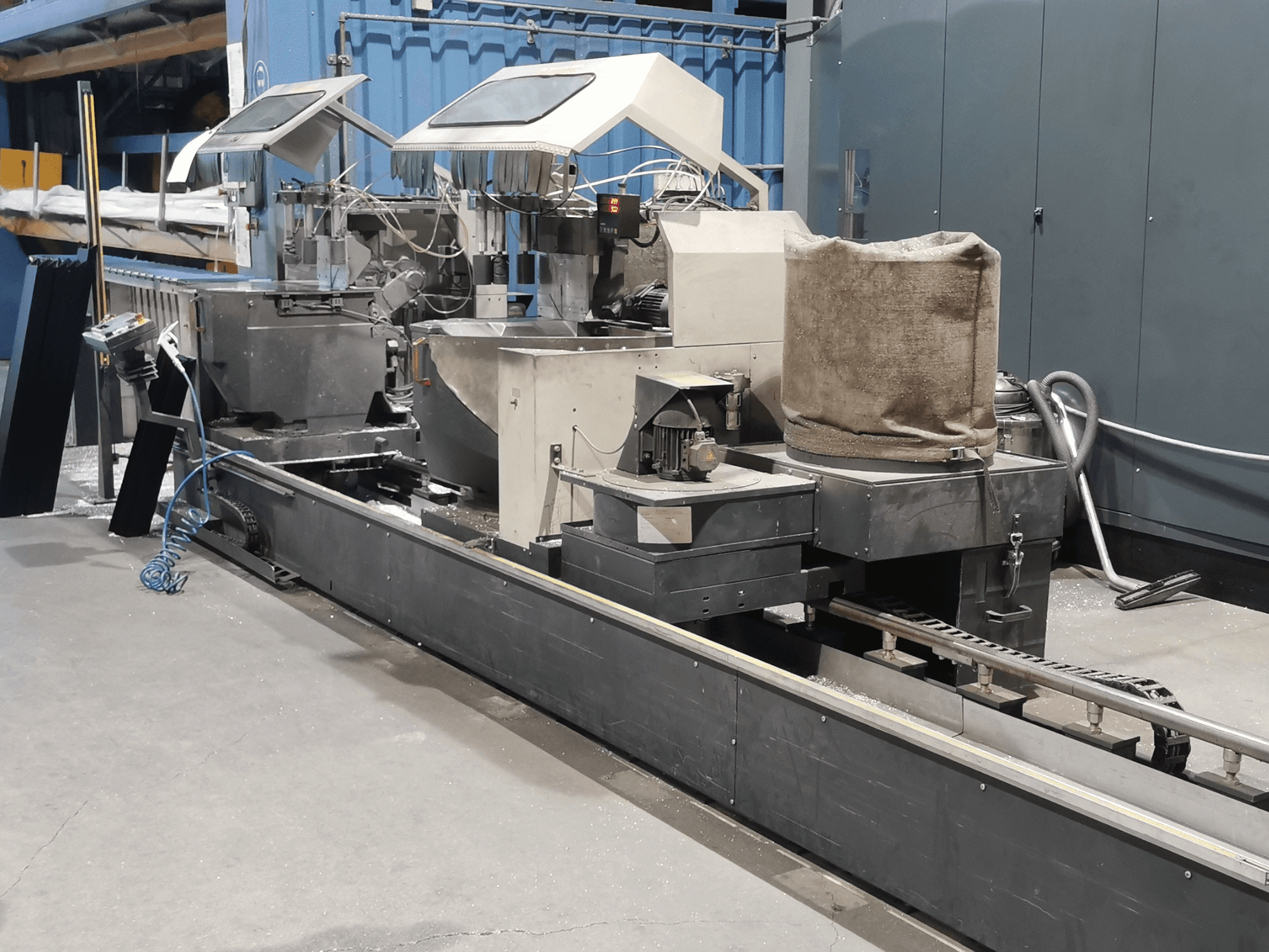 Industriell bearbetningsmaskin sedd från sidan, med trattar, transportband och kontrollpanel, i en fabriksmiljö.