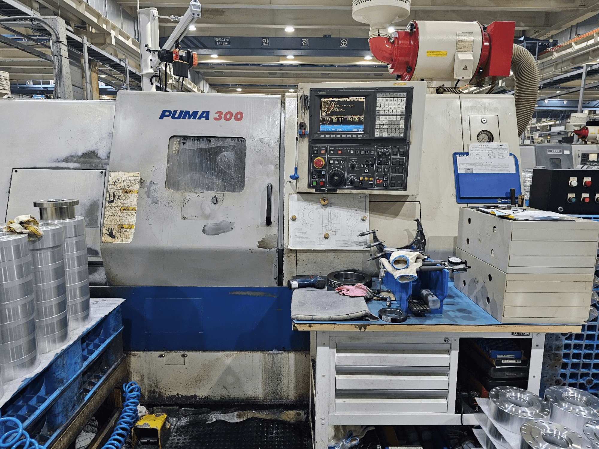 PUMA 300 CNC-maskin i en verkstad; framifrån med kontrollpanel, verktyg och metalldelar på en arbetsbänk.