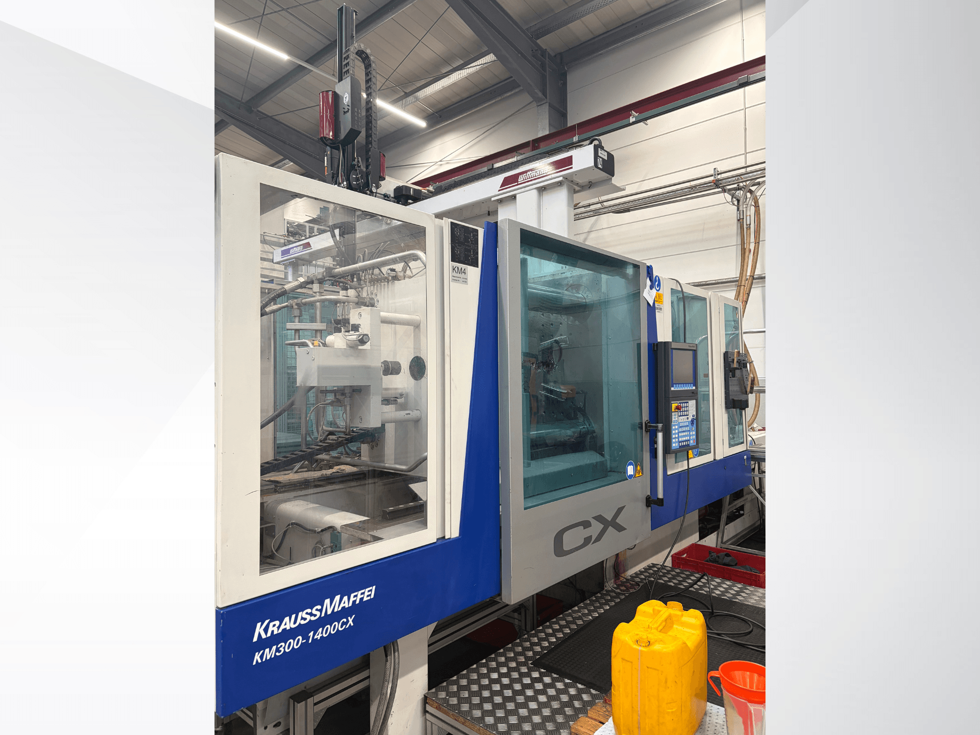 Krauss Maffei 300-1400 CX hydraulisk formsprutningsmaskin, framifrån sett med kontrollpanel och genomskinligt skyddshölje.