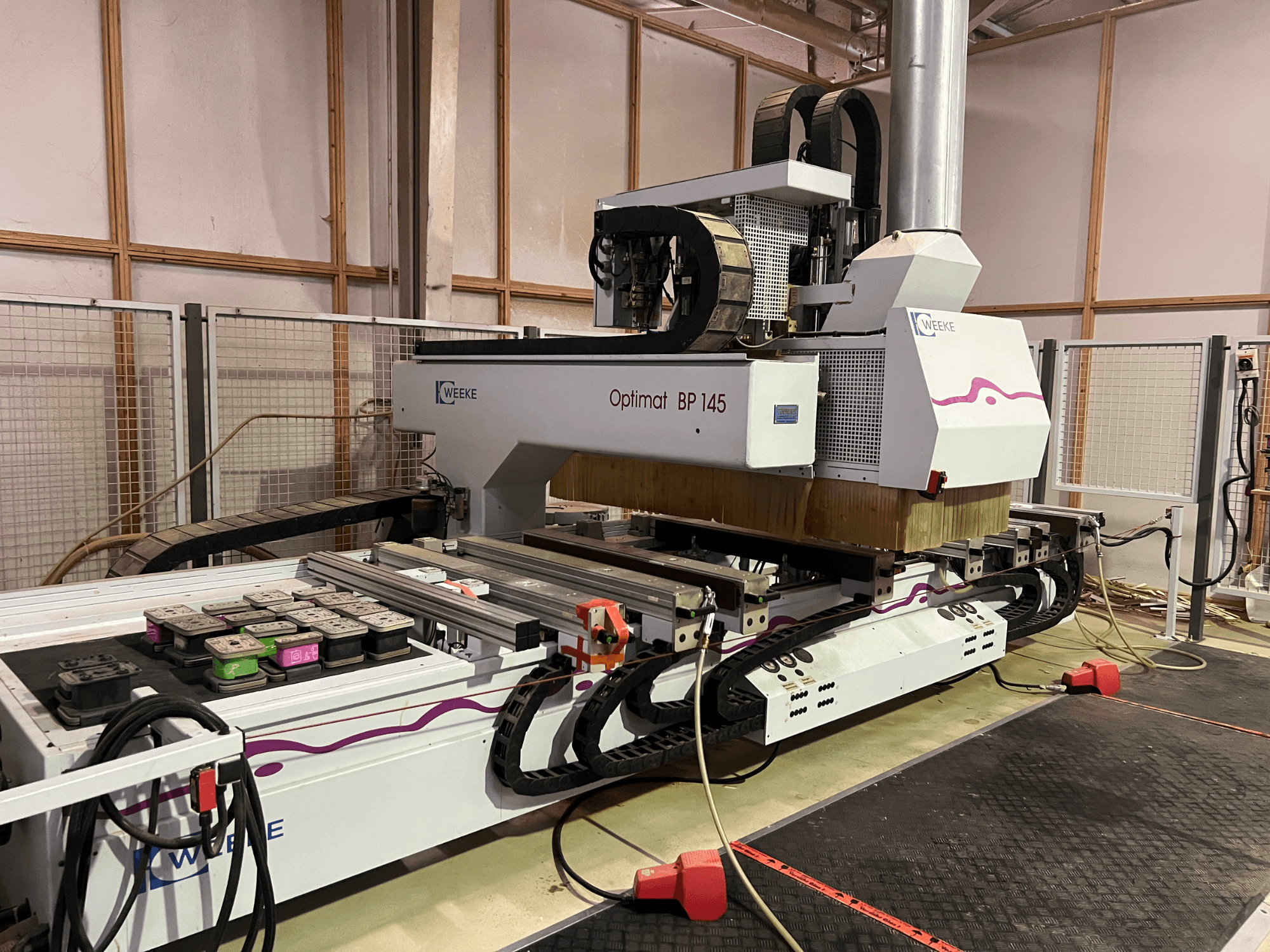 WEEKE Optimat BP 145 i en fabrik, visar en CNC-maskin med styrknappar och kablar, sedd från sidan.