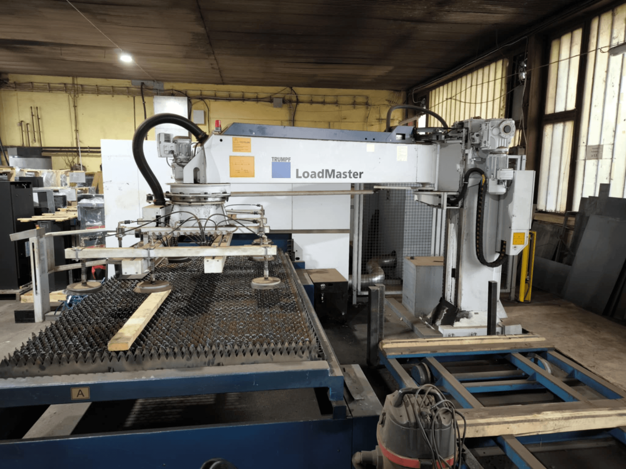 TRUMPF TRULASER 3030 FIBER skärmaskin, framifrån, med LoadMaster-system och placerad på ett gallerförsett arbetsbord.