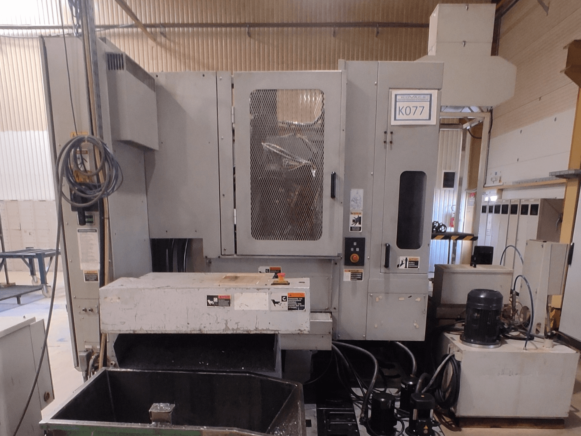 Grå CNC-maskin för industriellt bruk med stort arbetsbord, vy från sidan, med kontrollpanel och kylvätskebehållare, modell K077.
