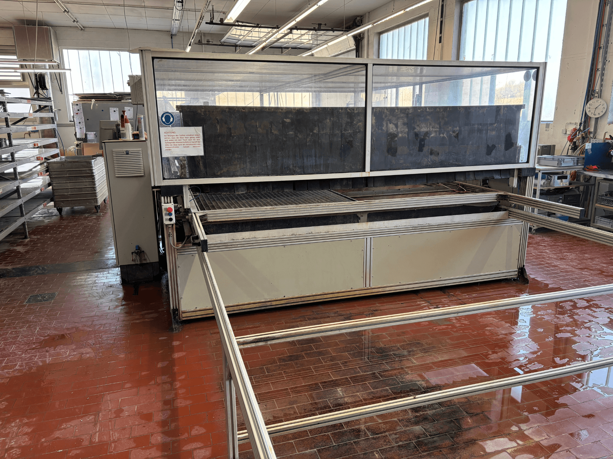 Vattenstråleskärmaskinen EXPERT SYSTEMTECHNIK cutExpert variojet i en verkstad, sett framifrån, med ett stort genomskinligt skydd.