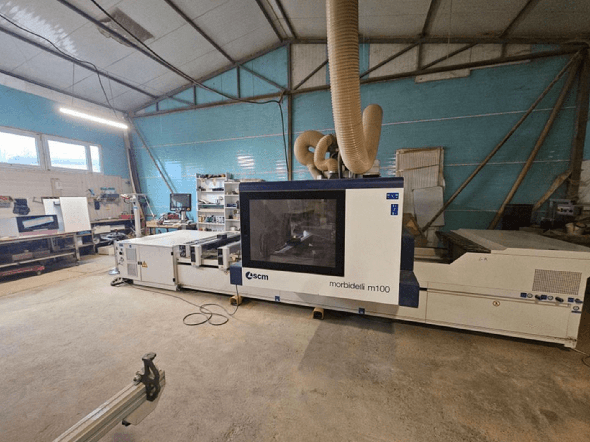 SCM MORBIDELLI M 100 CNC-bearbetningscenter i en verkstad, framifrån sett med dammutsug och omgivande arbetsutrustning.