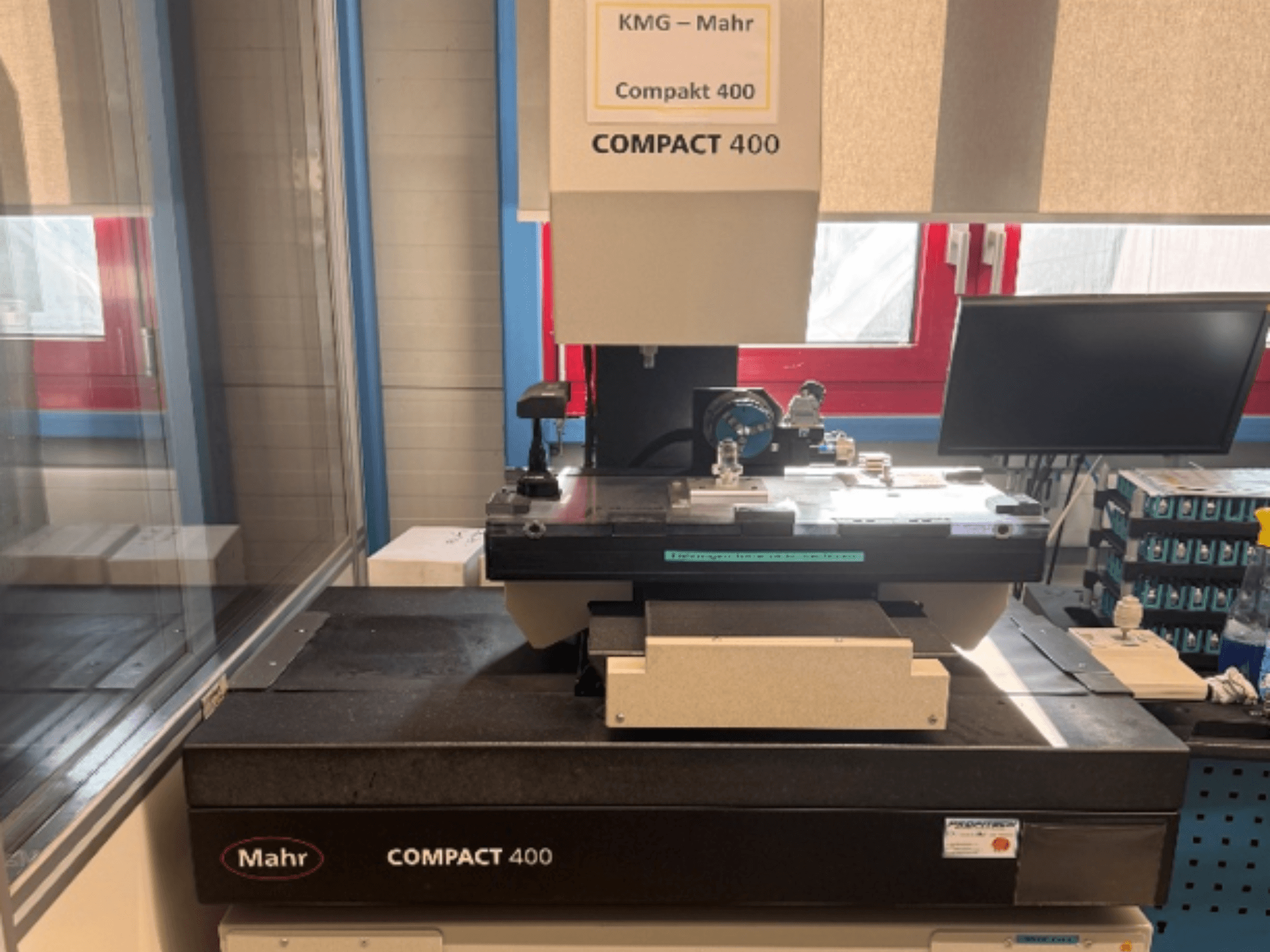 Koordinatmätmaskinen MAHR Compakt 400 sedd framifrån, med mätkomponenter och en bildskärm i närheten.