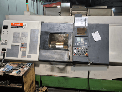 Mazak Integrex 200Y svarv, vy framifrån, med kontrollpanel och verktyg på en bänk. Synliga mätare och displayskärm.