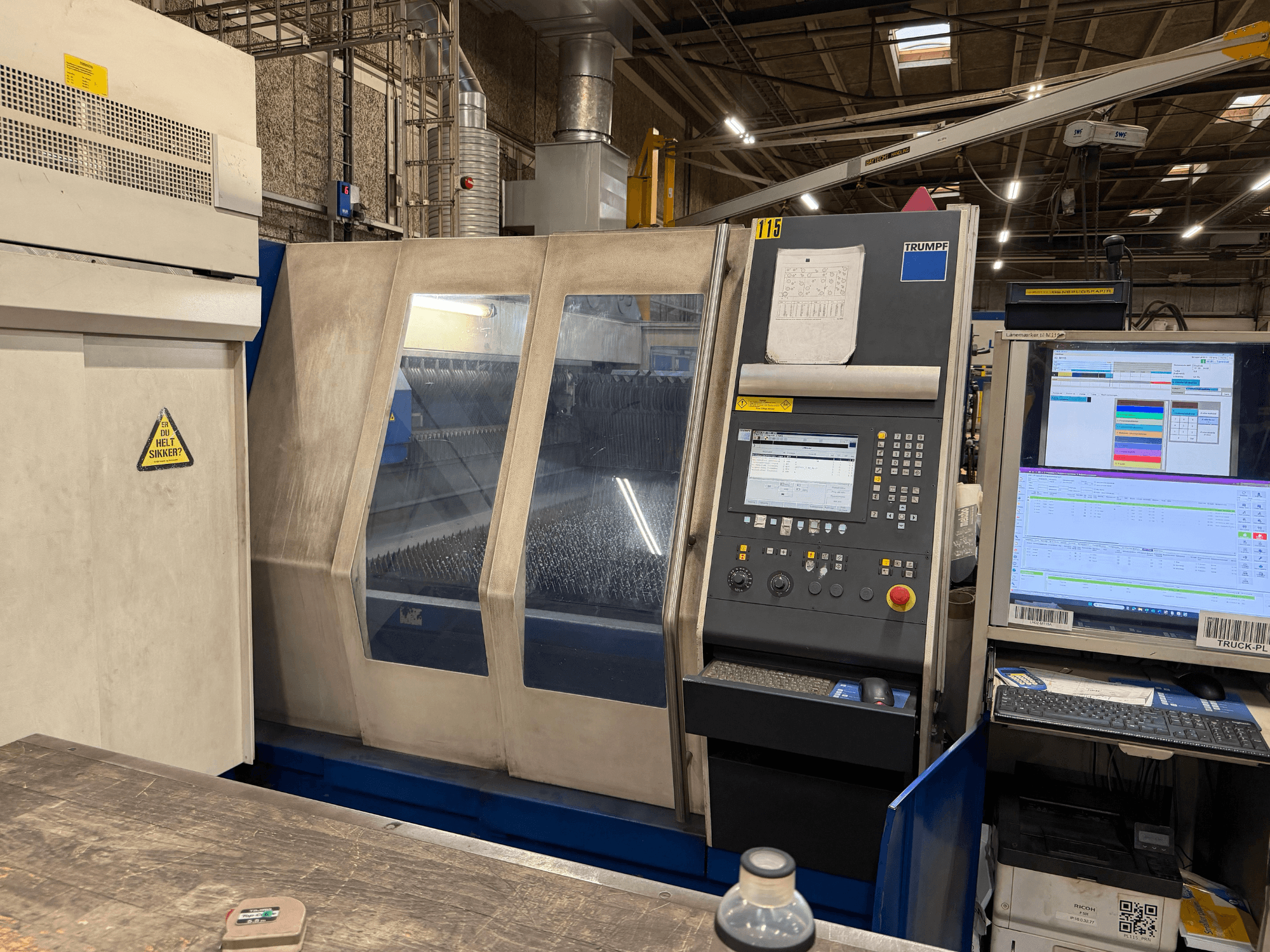 Frontvy av en industriell lasermaskin från Trumpf med kontrollpanel och digitala displayer, placerad i en fabriksmiljö.