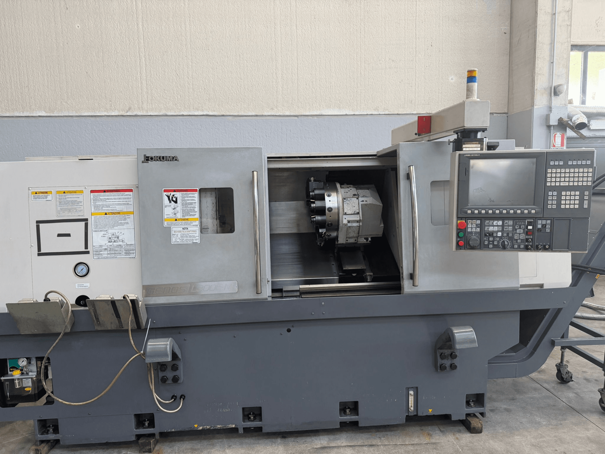 Okuma CNC-svarv, framifrån, med kontrollpanel, hållare för skärverktyg och säkerhetsvarningar på sidan.