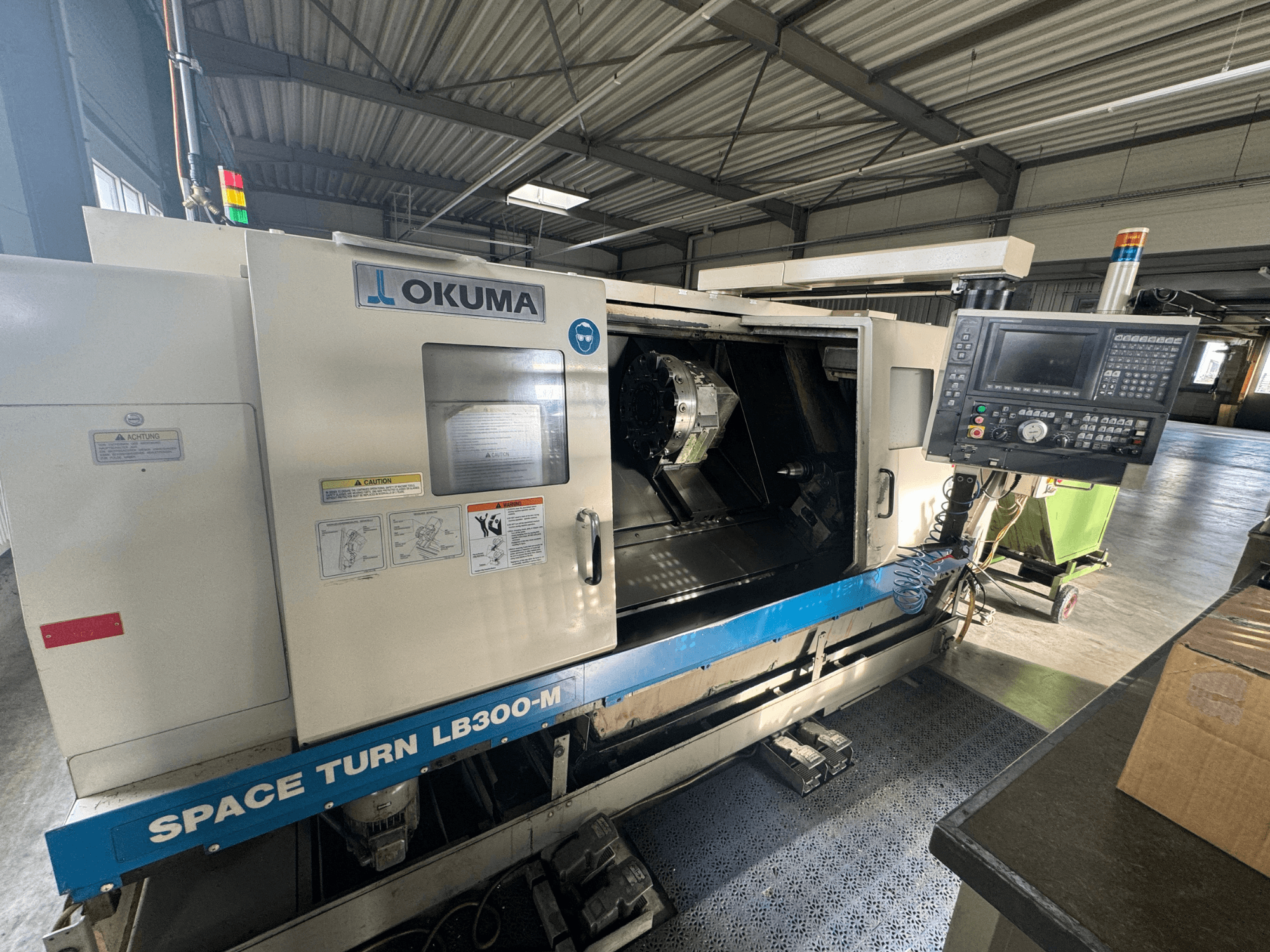 Okuma Space Turn LB300-M CNC-svarv framifrån, med kontrollpanel och öppen dörr som avslöjar det inre bearbetningsområdet.