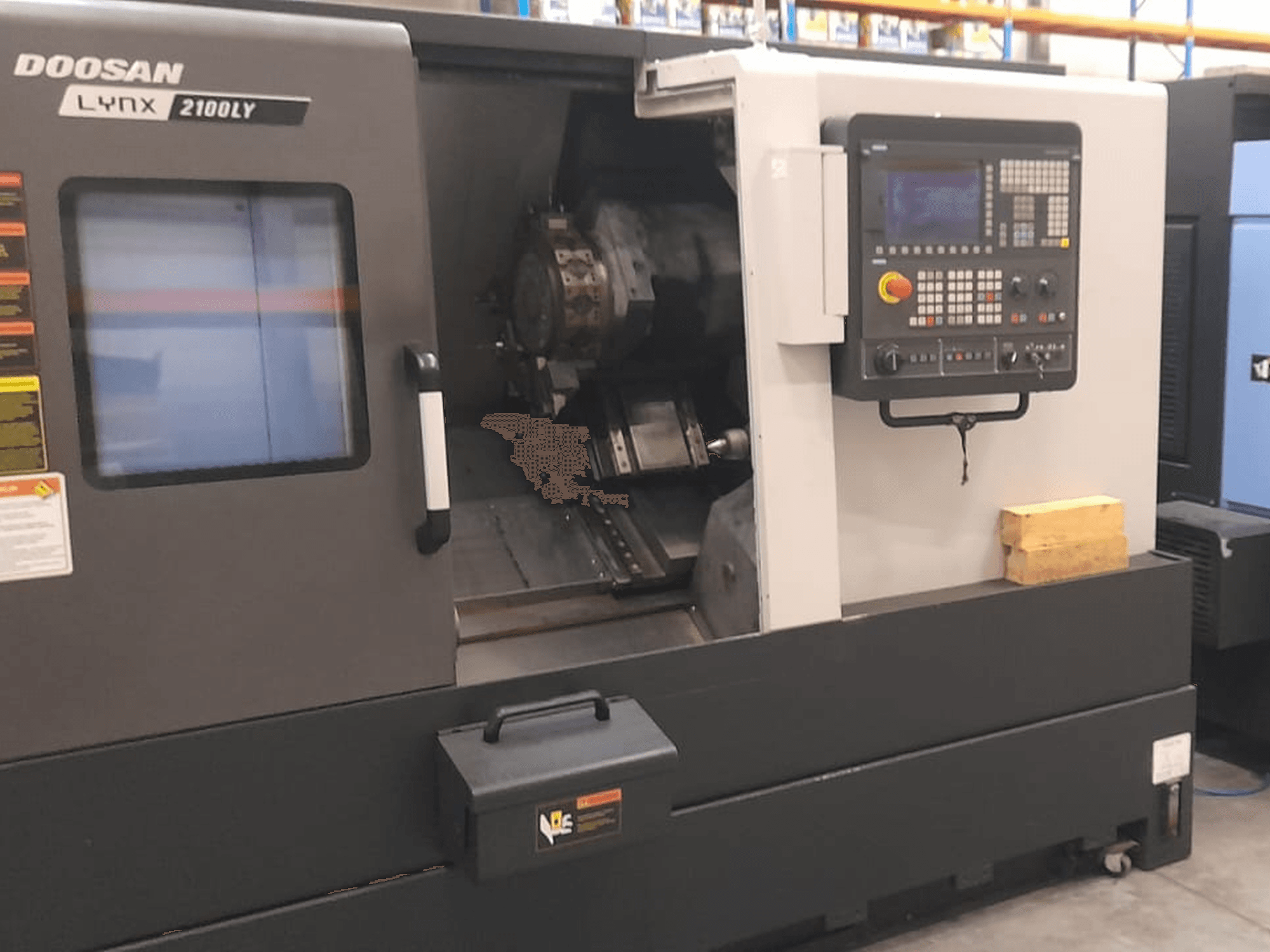 Doosan Lynx 2100LY CNC-svarv, framifrån med kontrollpanel, verktygshållare och invändigt arbetsutrymme; tekniska etiketter synliga.