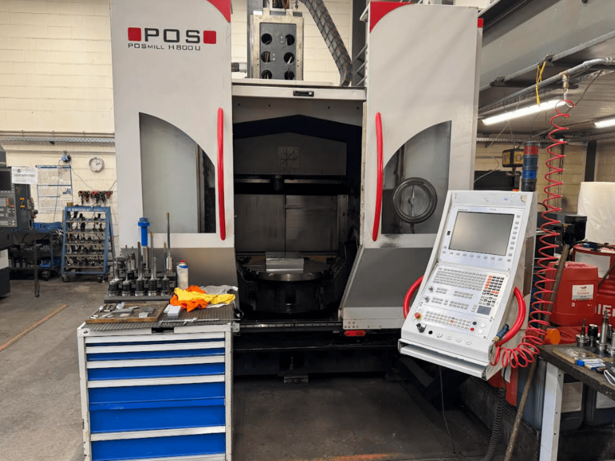 CNC-maskinen POSMILL H800 U sedd framifrån, med kontrollpanelen och arbetsområdet med verktyg och utrustning i närheten.