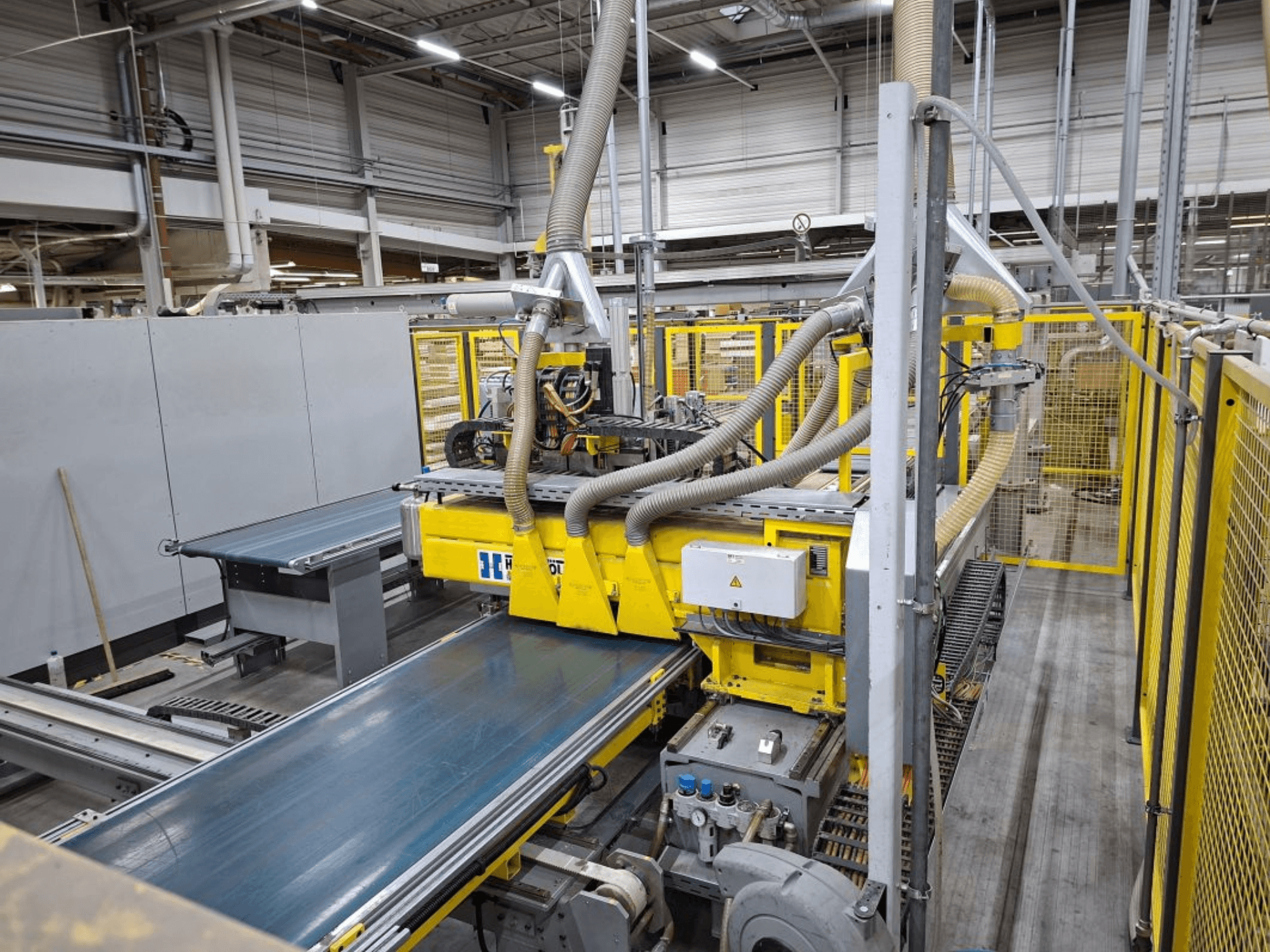 Industriellt transportsystem sett från sidan, med gula maskiner, kontrollpanel och slangfästen för tillverkning.