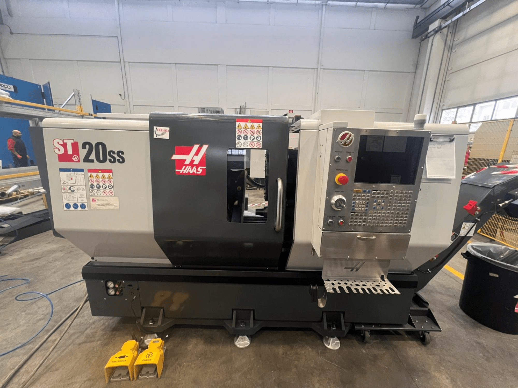 Haas ST 20SS CNC-svarv i sidovy, med kontrollpanel, säkerhetsetiketter och fotpedaler på golvet.