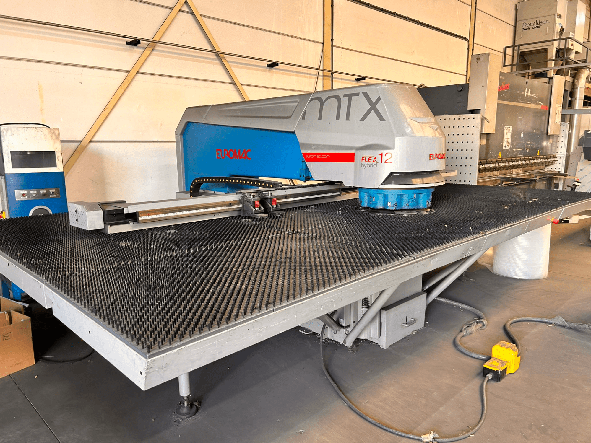 Euromac MTX FLEX 12 CNC-stansmaskin, framifrån, med ett stort perforerat bord och en kontrollpanel.