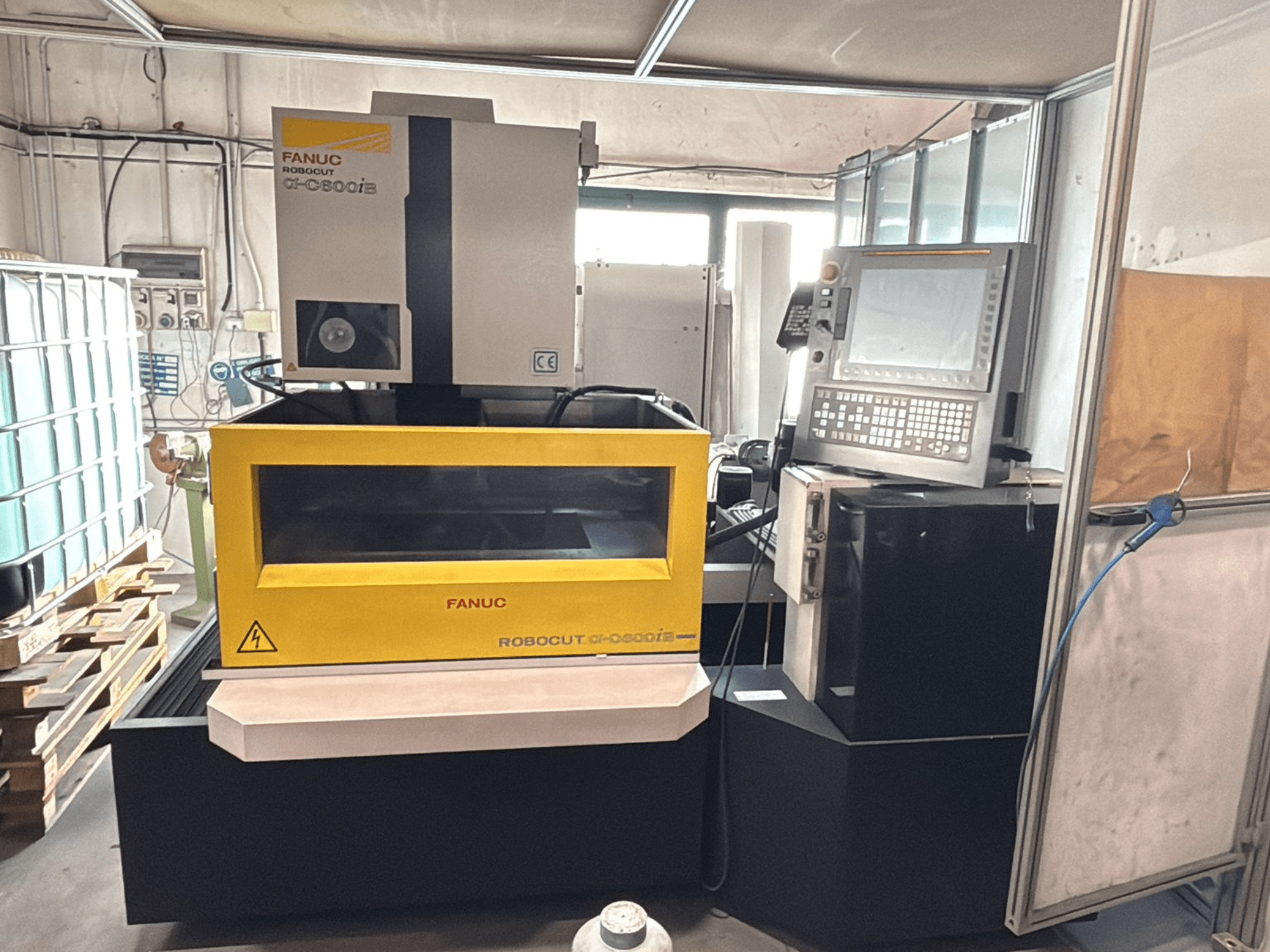 Frontvy av en FANUC Robocut α-0iE CNC-maskin med gult hölje som visar kontrollpanelen och displayen.