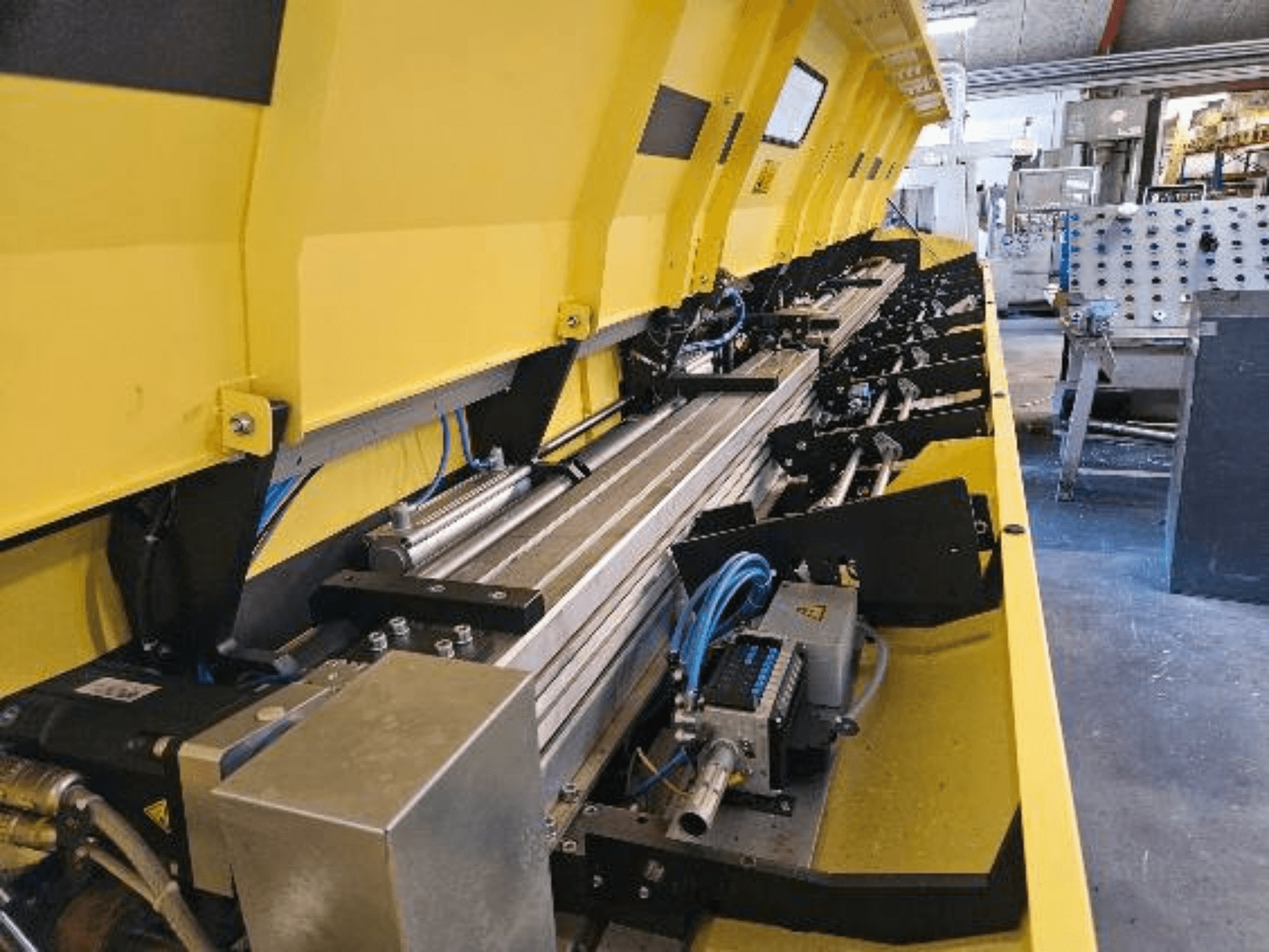 Närbild av en gul hydraulmaskin med metallkomponenter och transportband, med slangar och elektroniska delar.