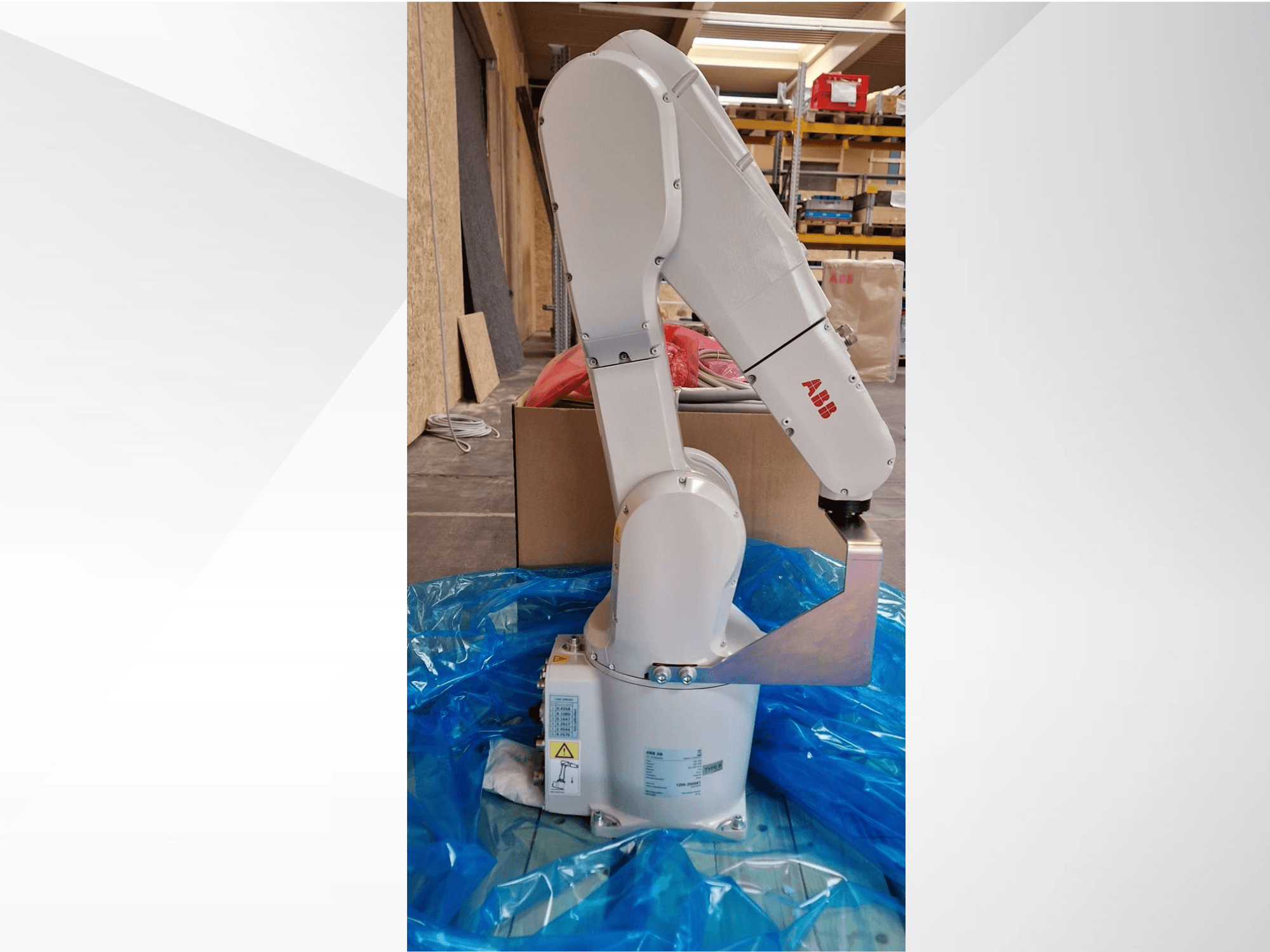 ABB robotarm modell, sidovy på blå presenning, visar ledade leder och metalleffektorer, med tekniska etiketter synliga.